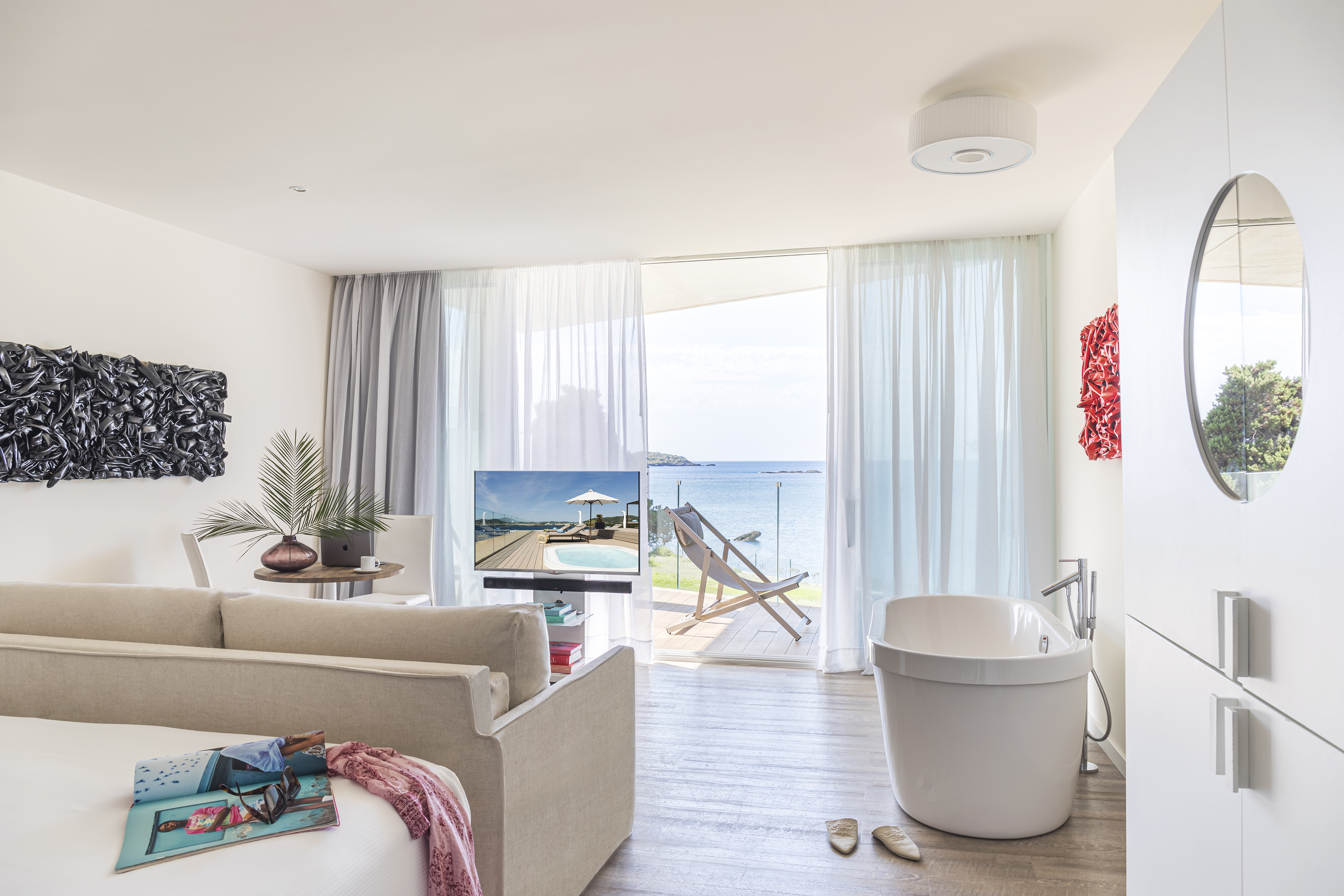 Luxury hotel suite with ocean view balcony and freestanding bathtub.