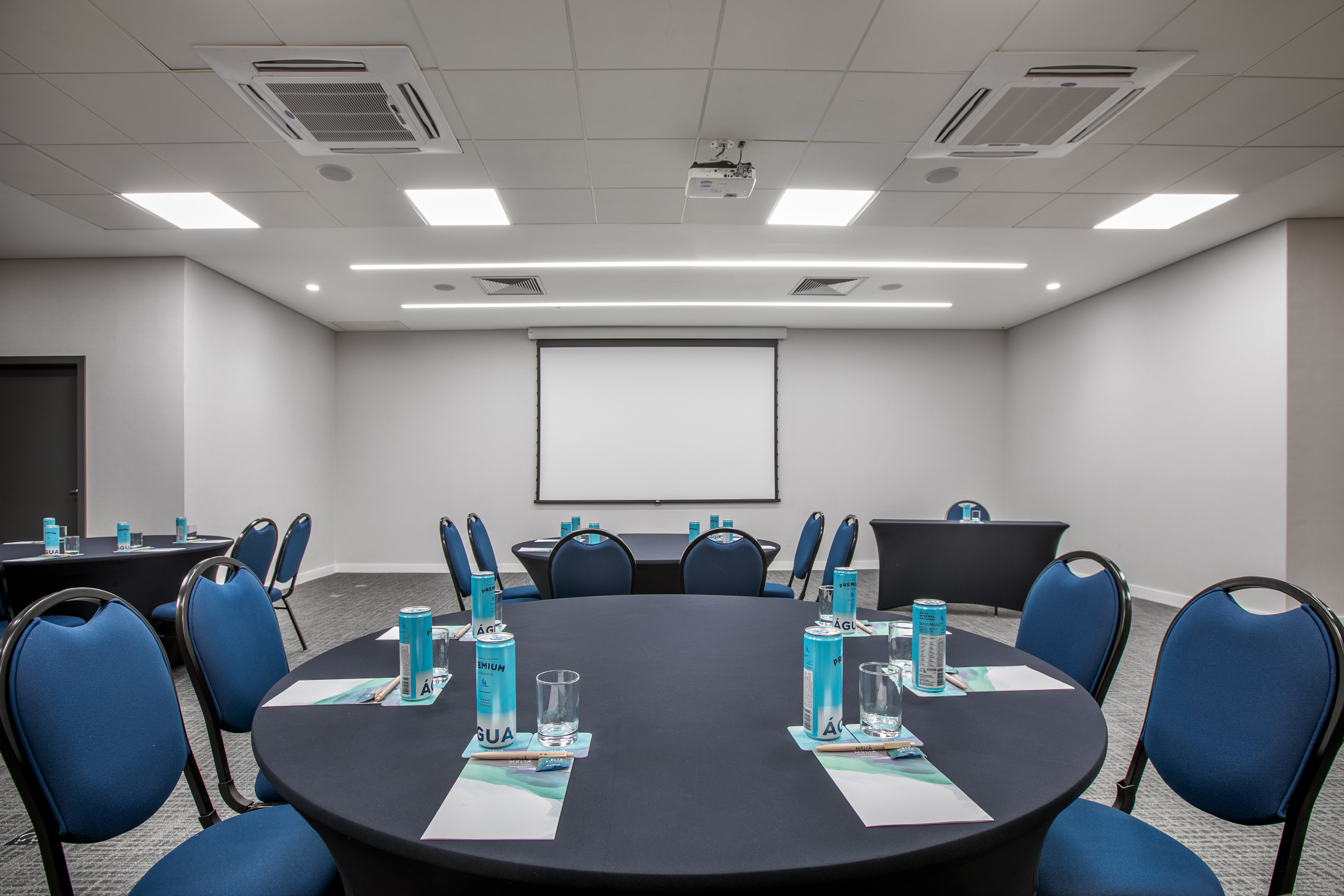 Modern conference room with round tables, blue chairs, projector screen.