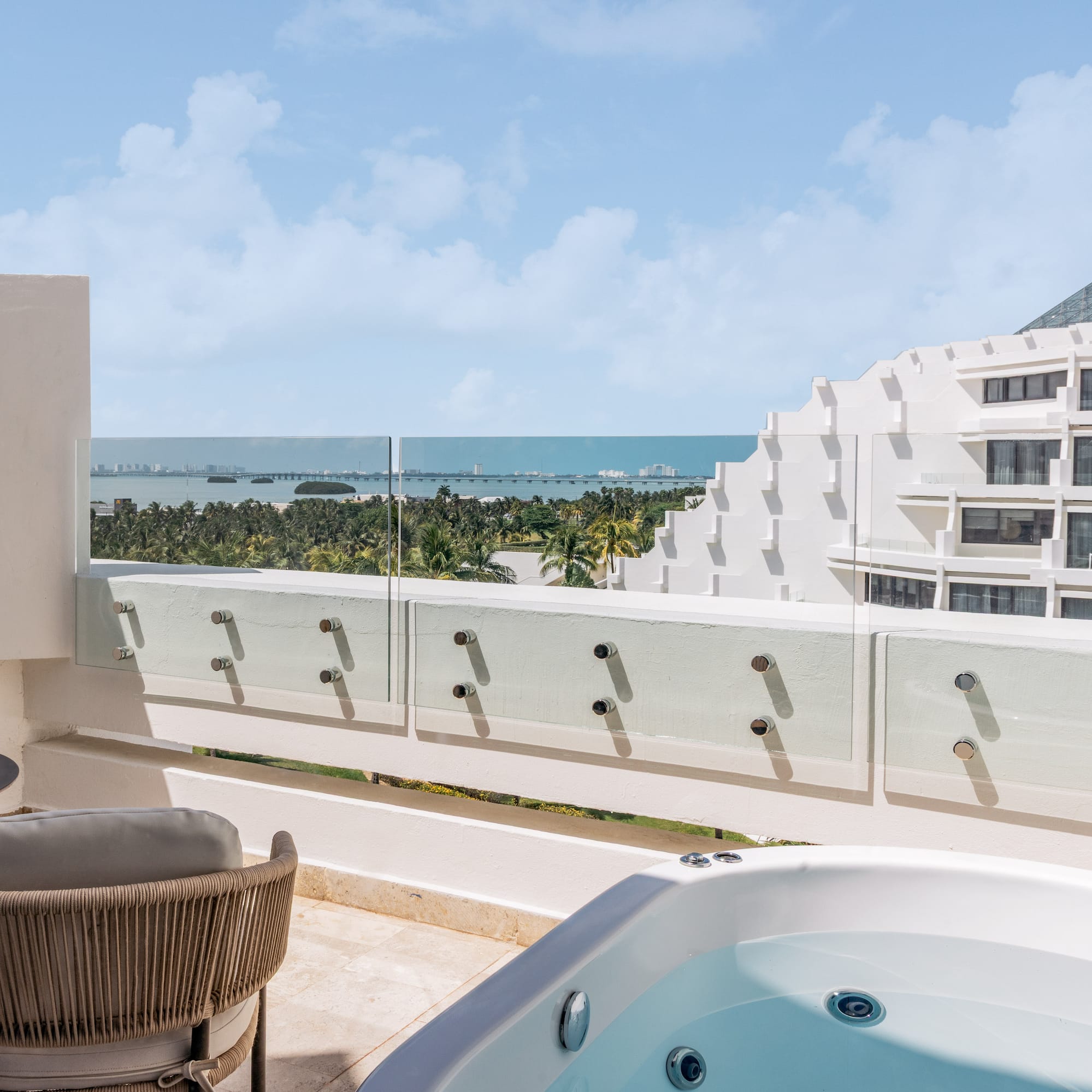 Luxury hotel balcony with outdoor hot tub and panoramic ocean view.