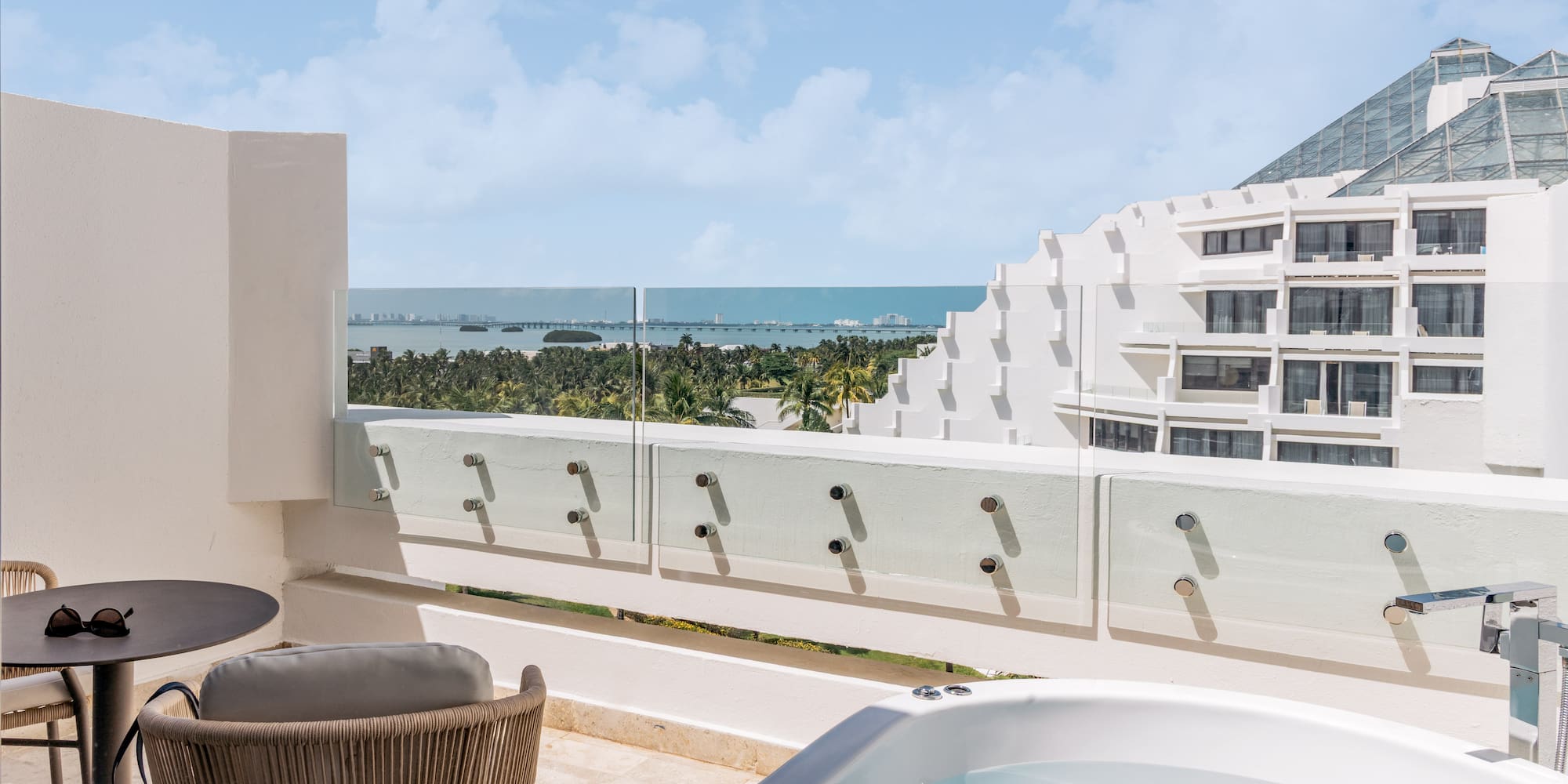 Luxury hotel balcony with outdoor hot tub and panoramic ocean view.