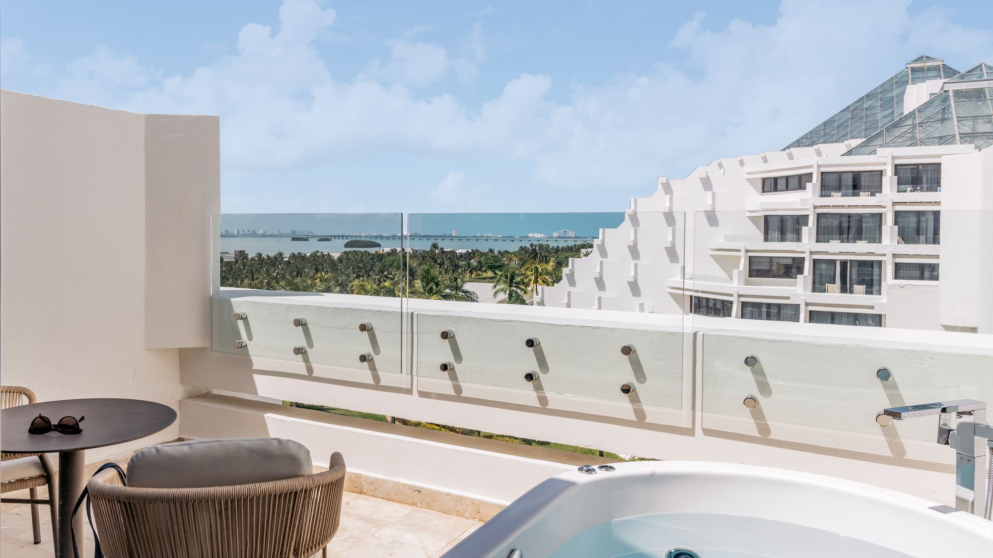 Luxury hotel balcony with outdoor hot tub and panoramic ocean view.