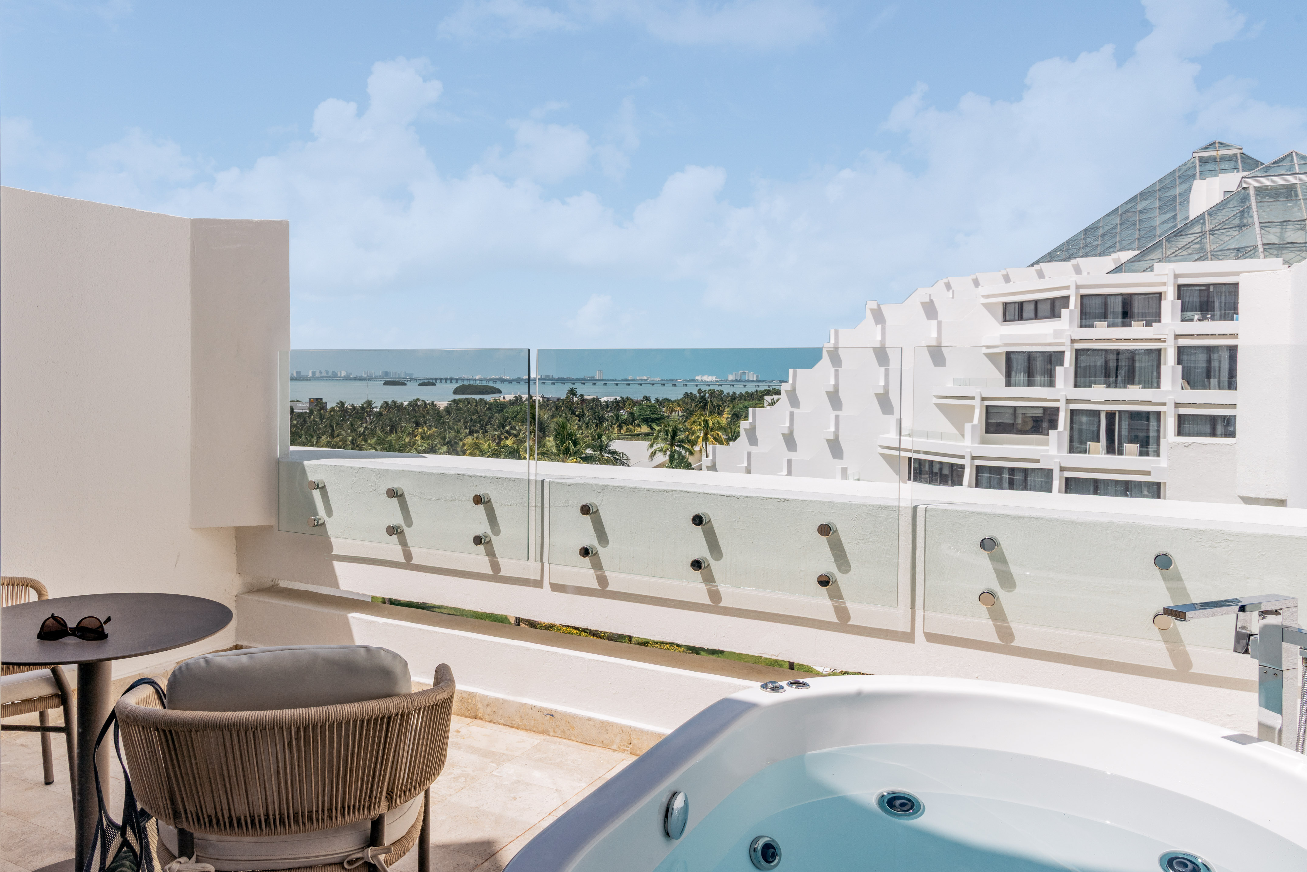 Luxury hotel balcony with outdoor hot tub and panoramic ocean view.
