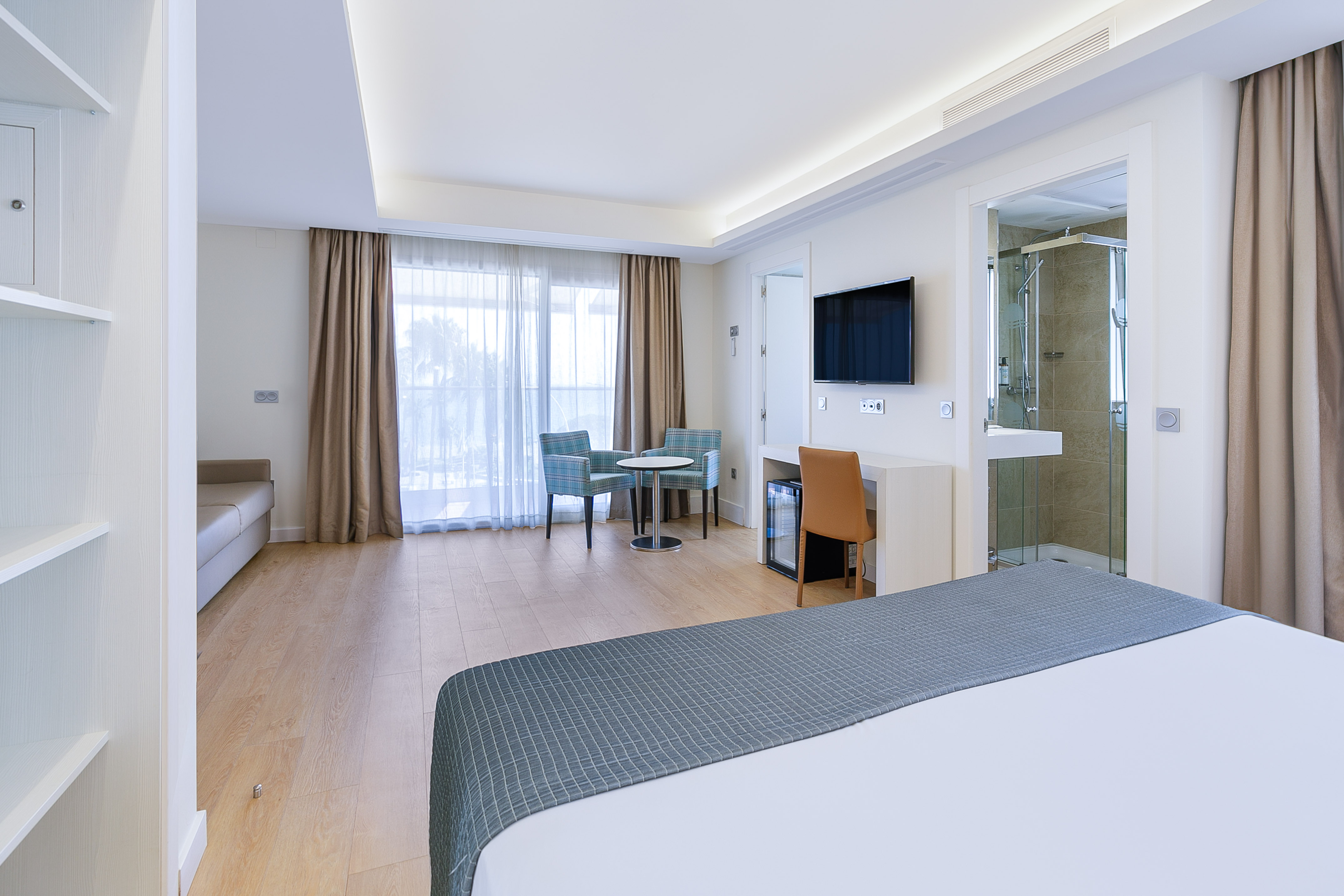 Modern hotel room with bed, seating, desk, TV, and balcony access.