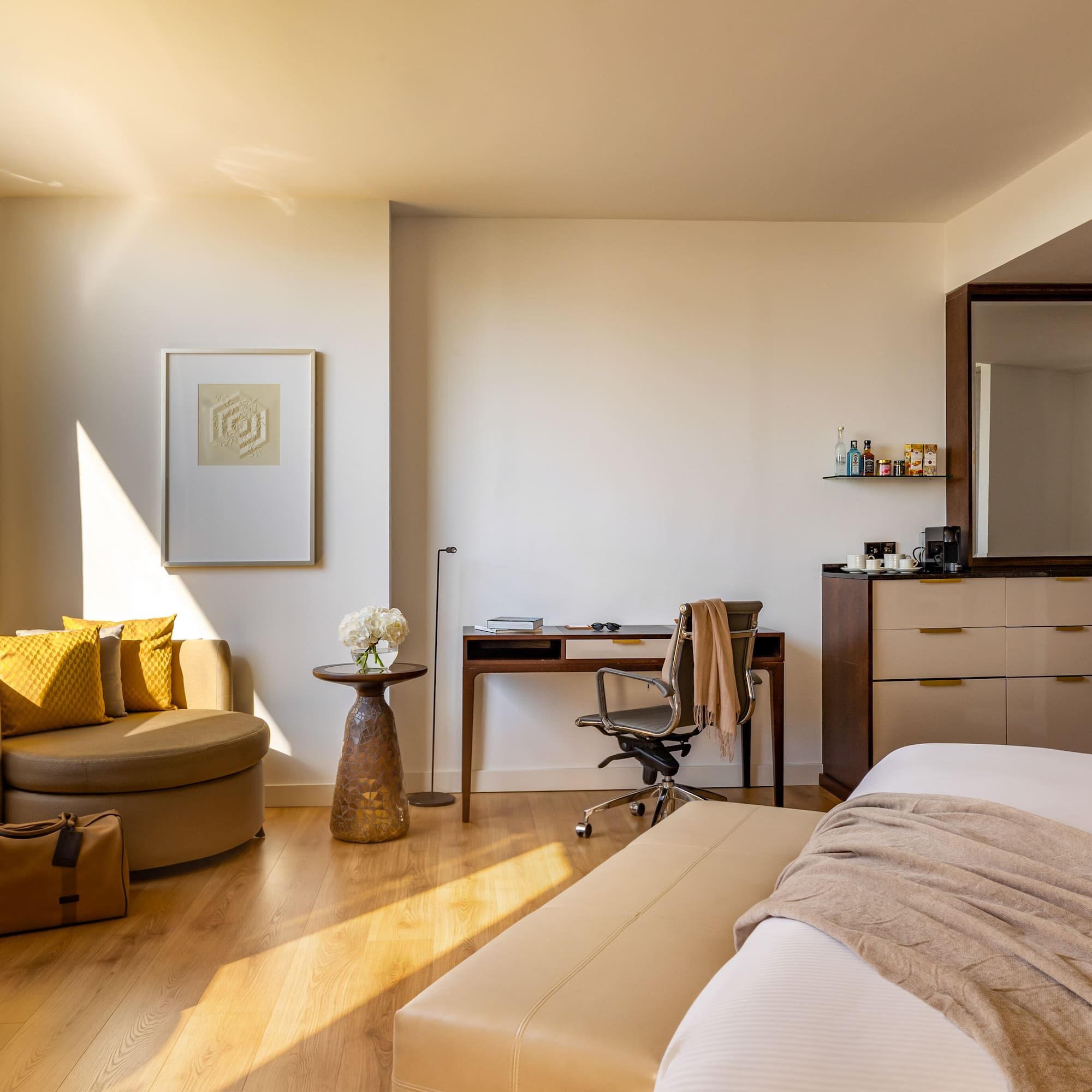 Sunny modern hotel room with bed, work desk, armchair, and city view.