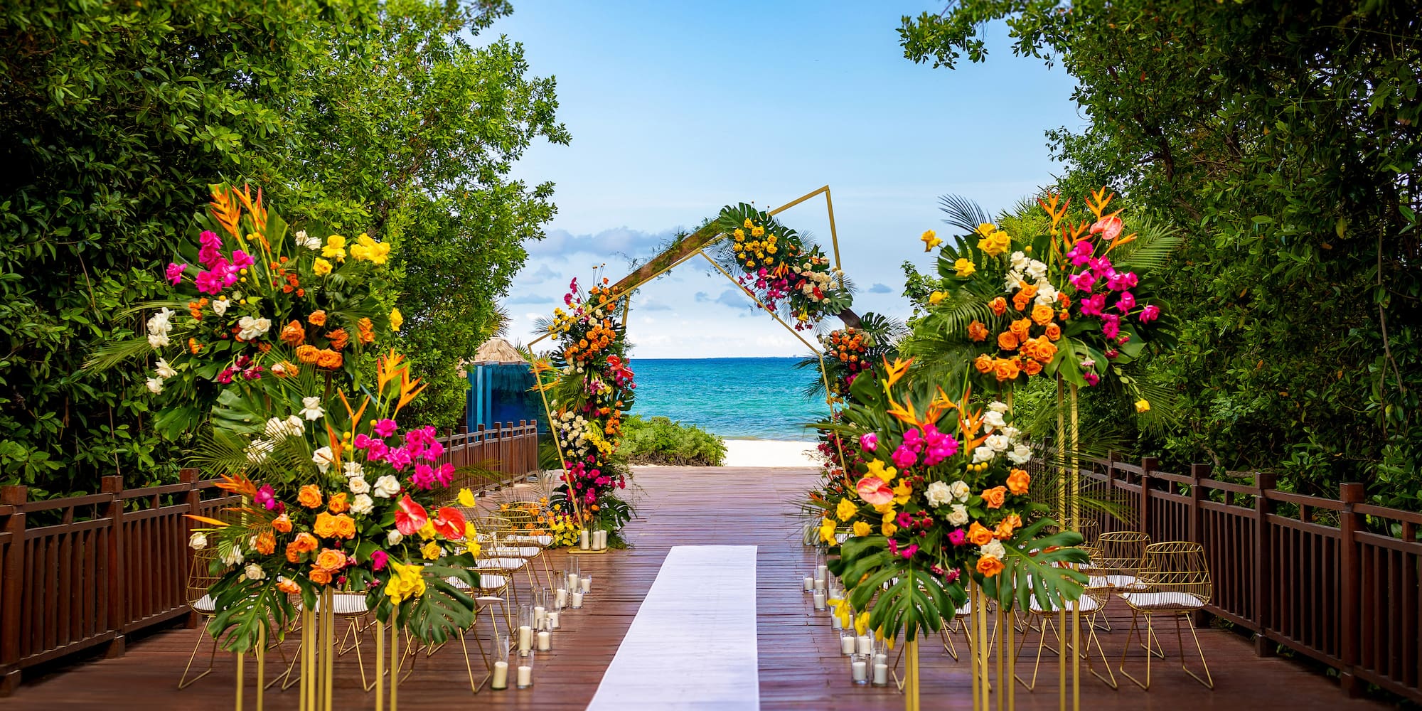 Tropical beach wedding: vibrant floral arch, white aisle, ocean view.