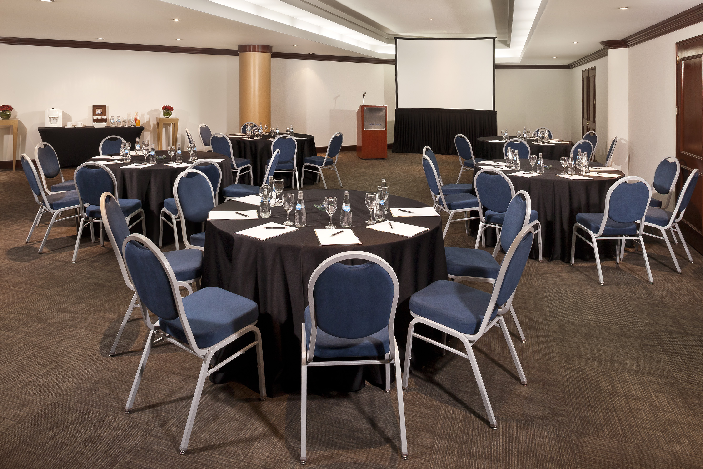 Hotel conference room with round tables, blue chairs, projector, and podium.