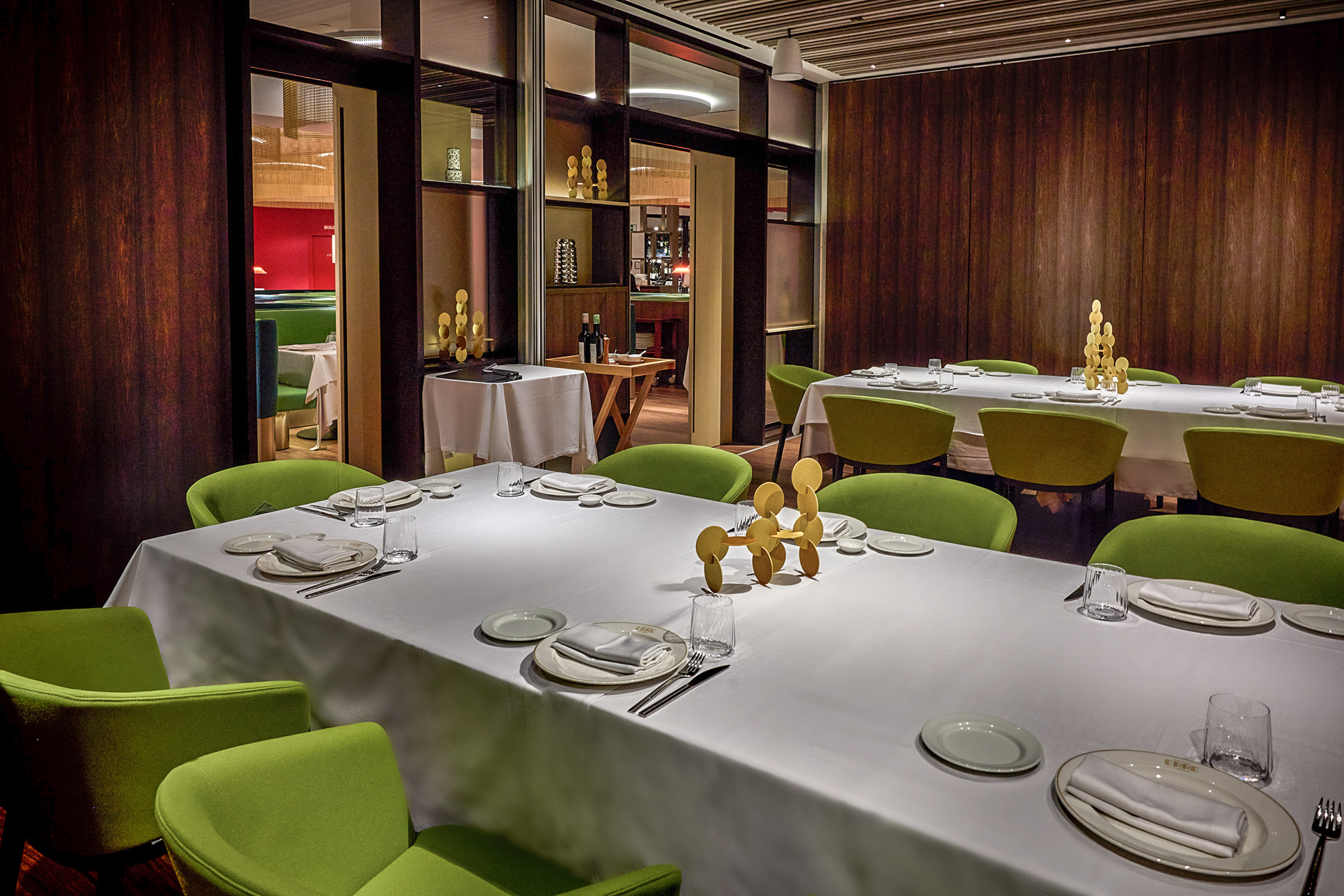 Elegant restaurant dining room with white tables, modern green chairs, wood walls.