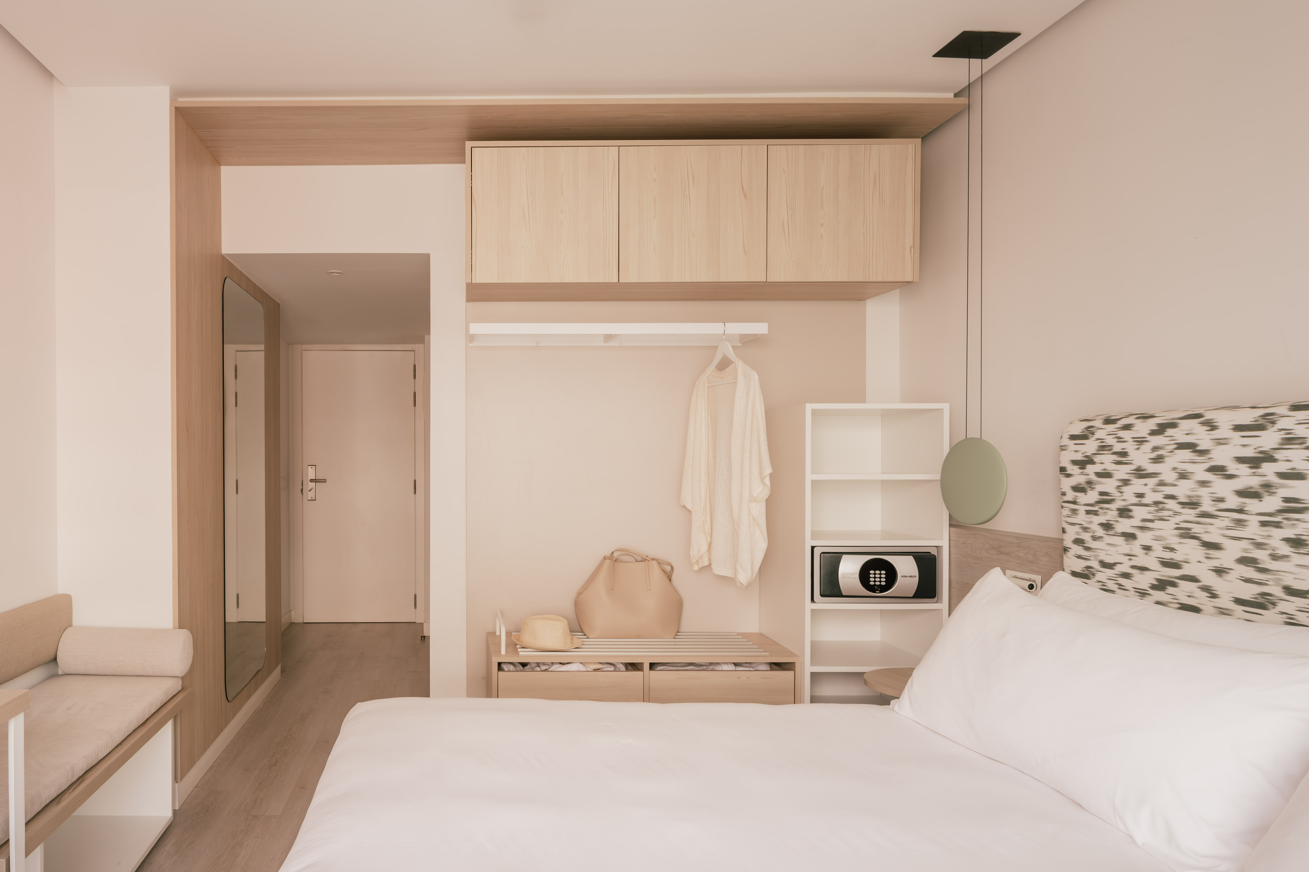 Habitación de hotel moderna con cama, cabecero, armario de madera y caja fuerte.