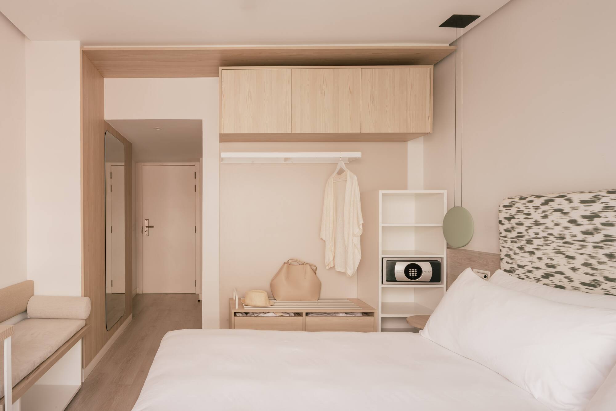 Habitación de hotel moderna con cama, cabecero, armario de madera y caja fuerte.