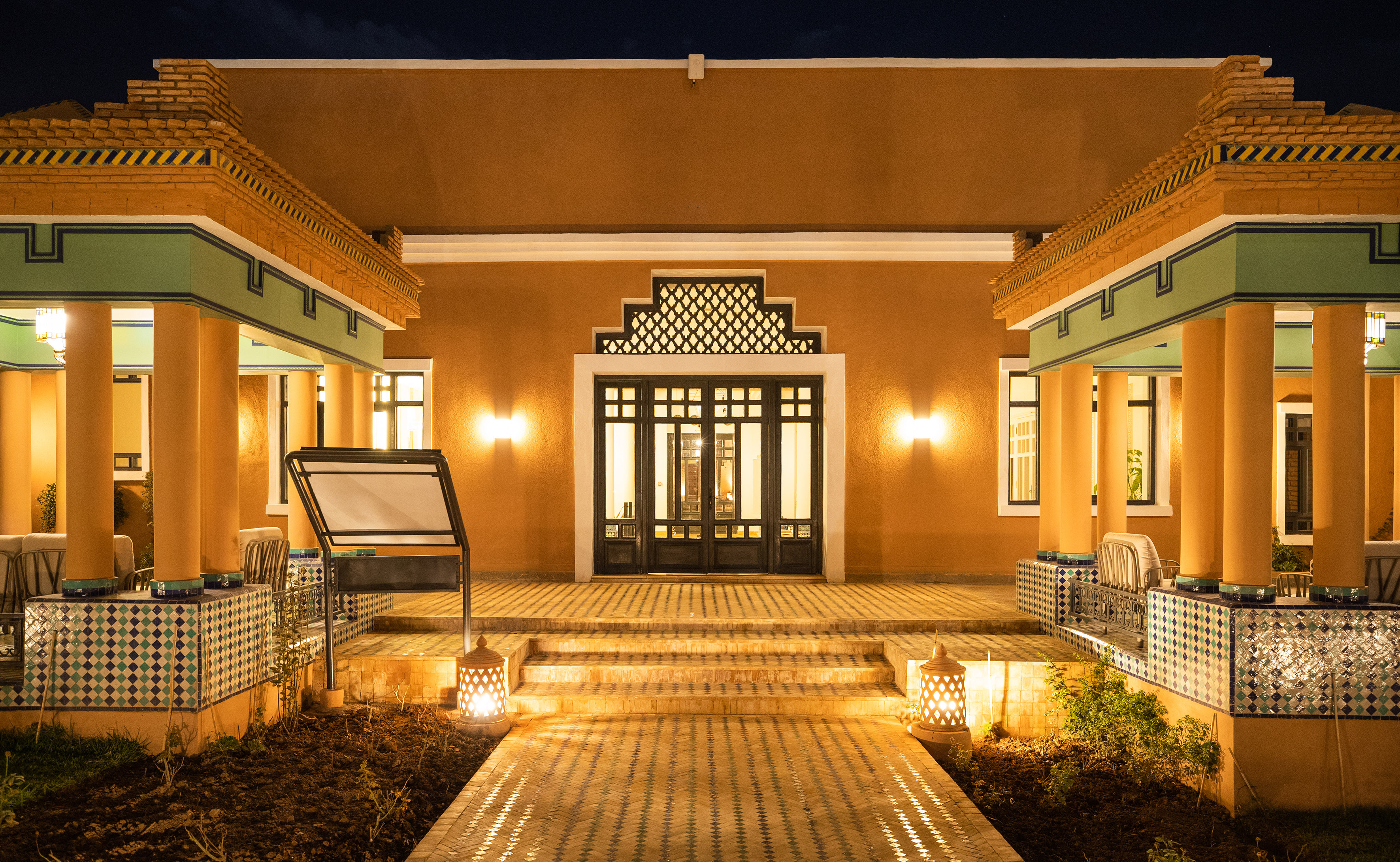 Moroccan architecture: illuminated entrance, ornate doors, tiled patio at night.