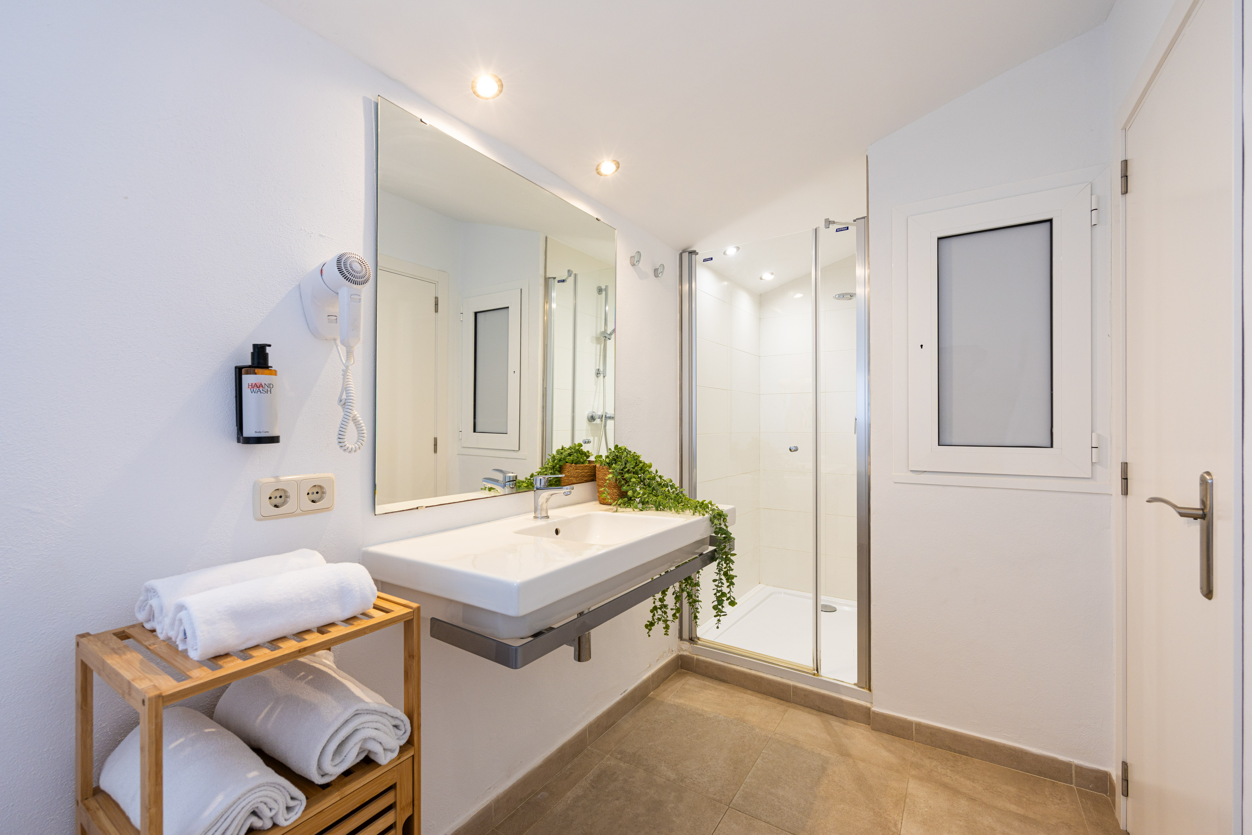 White bathroom with modern sink, large mirror, shower, and fresh towels.