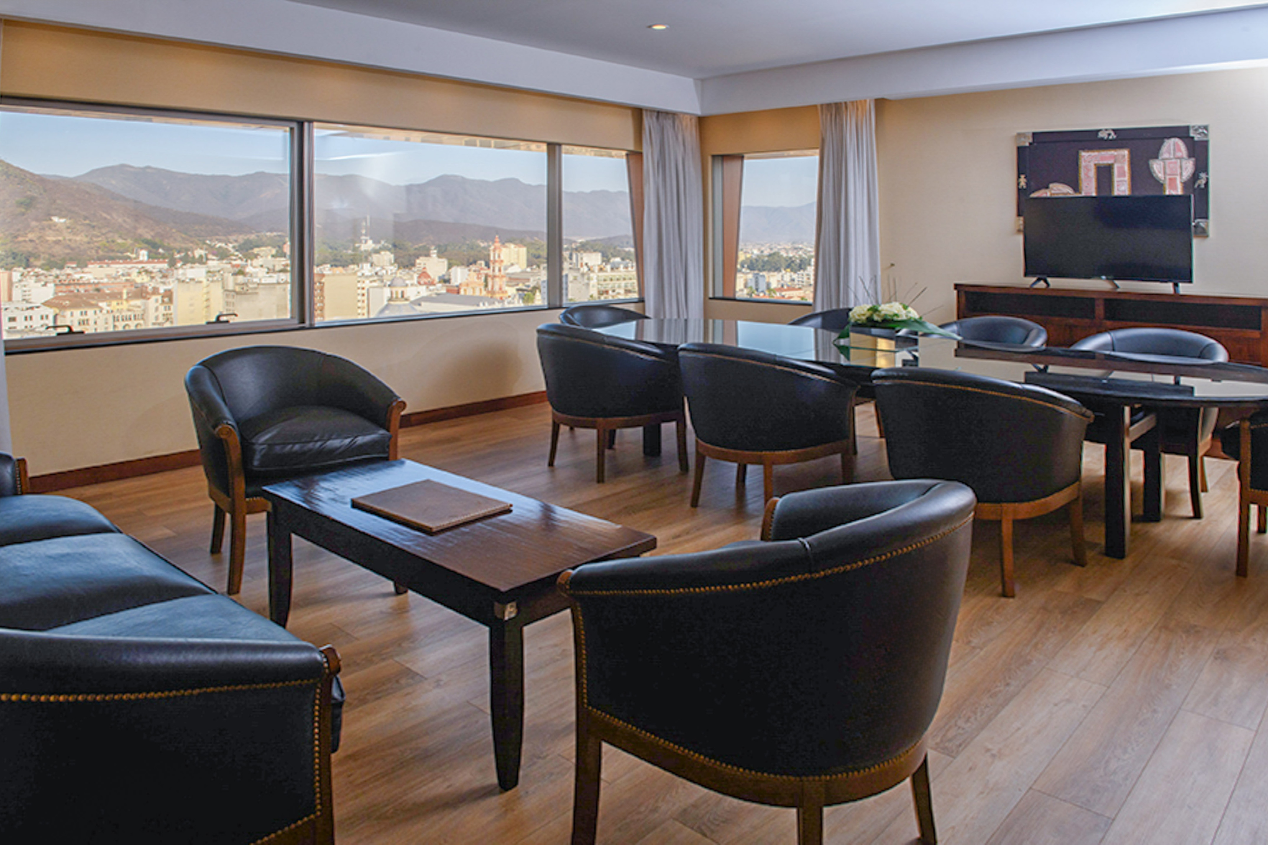 Business meeting room with panoramic city & mountain view, black leather chairs.