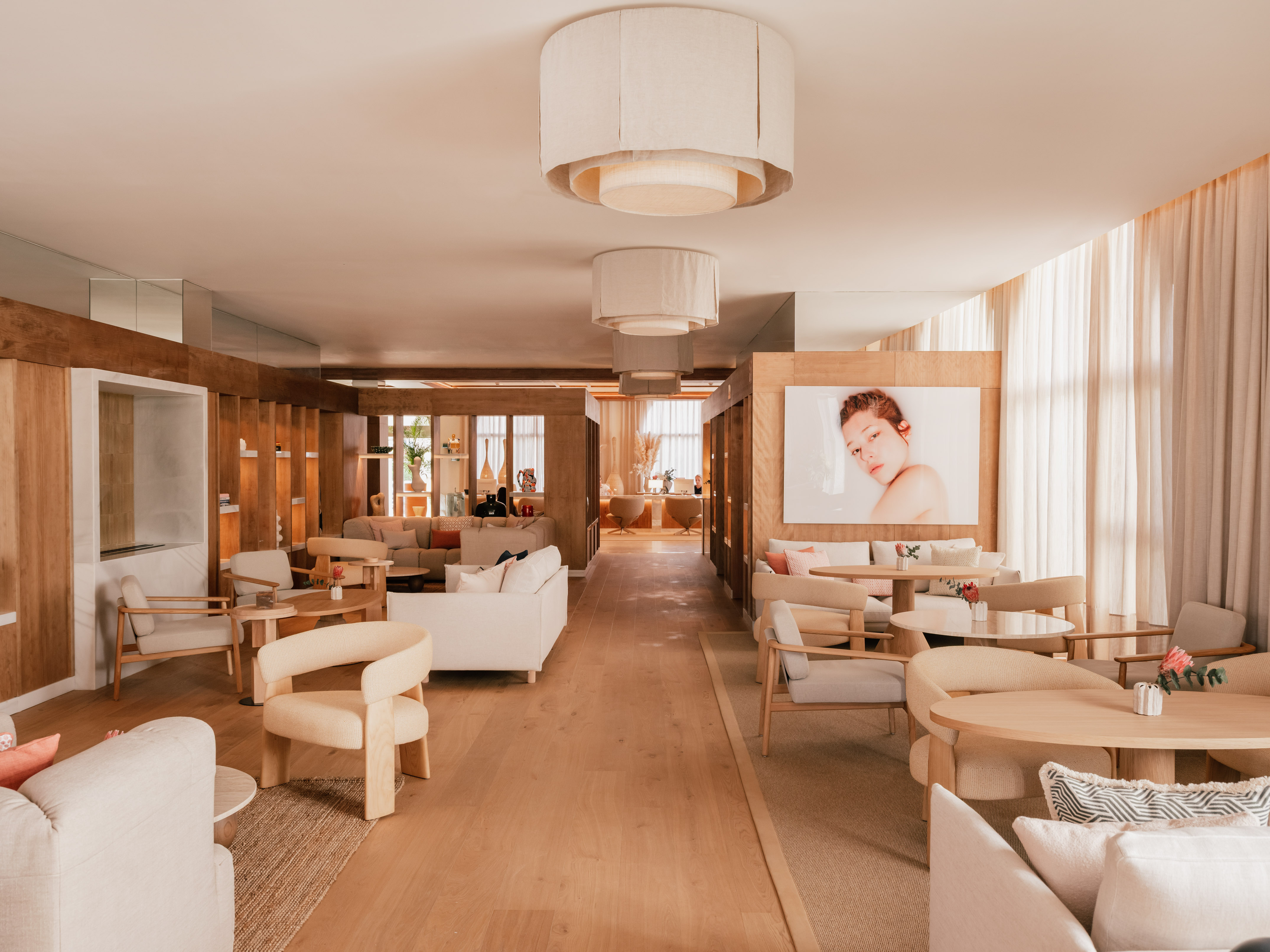 Modern lounge with neutral tones, light wood, inviting seating, and ceiling lamps.
