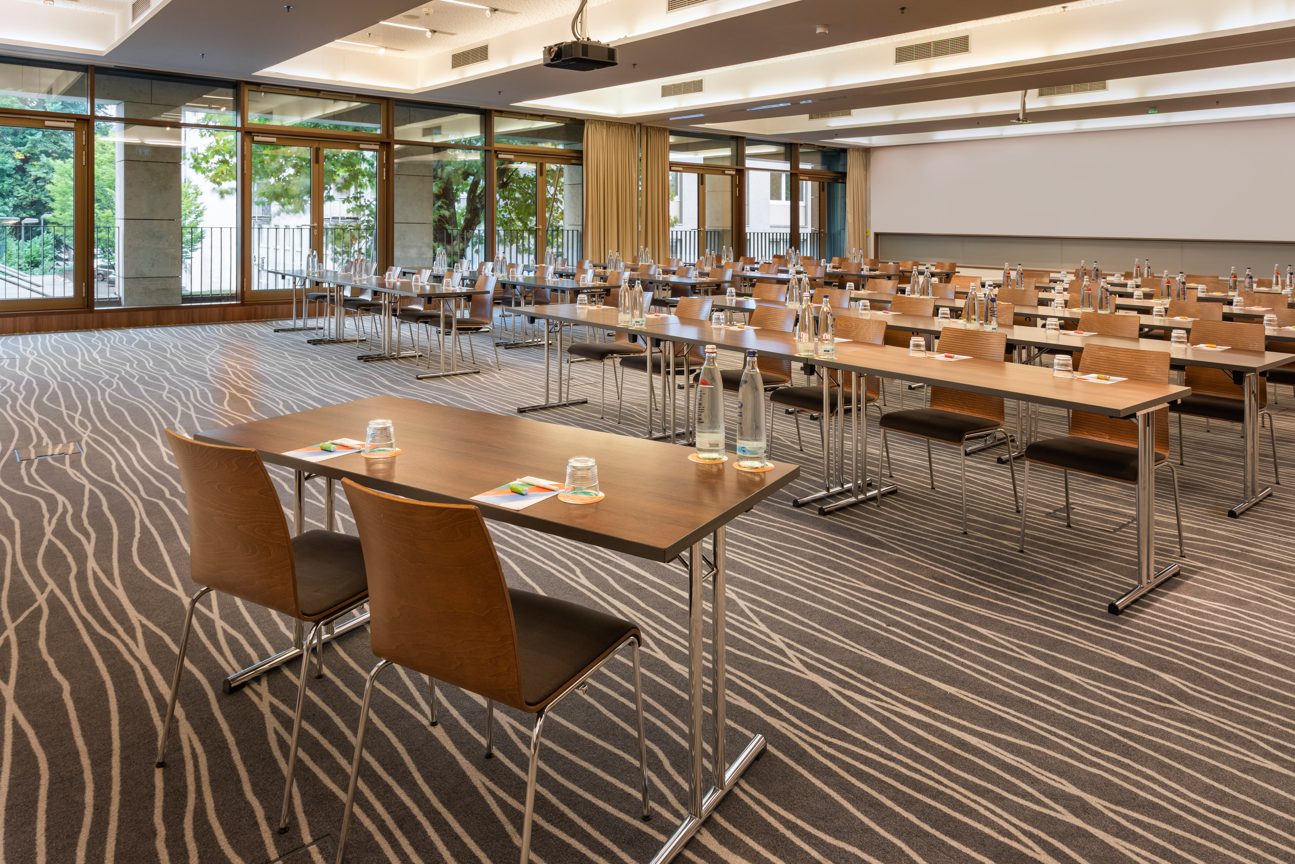Conference room setup: tables, chairs, projector, screen, large windows.