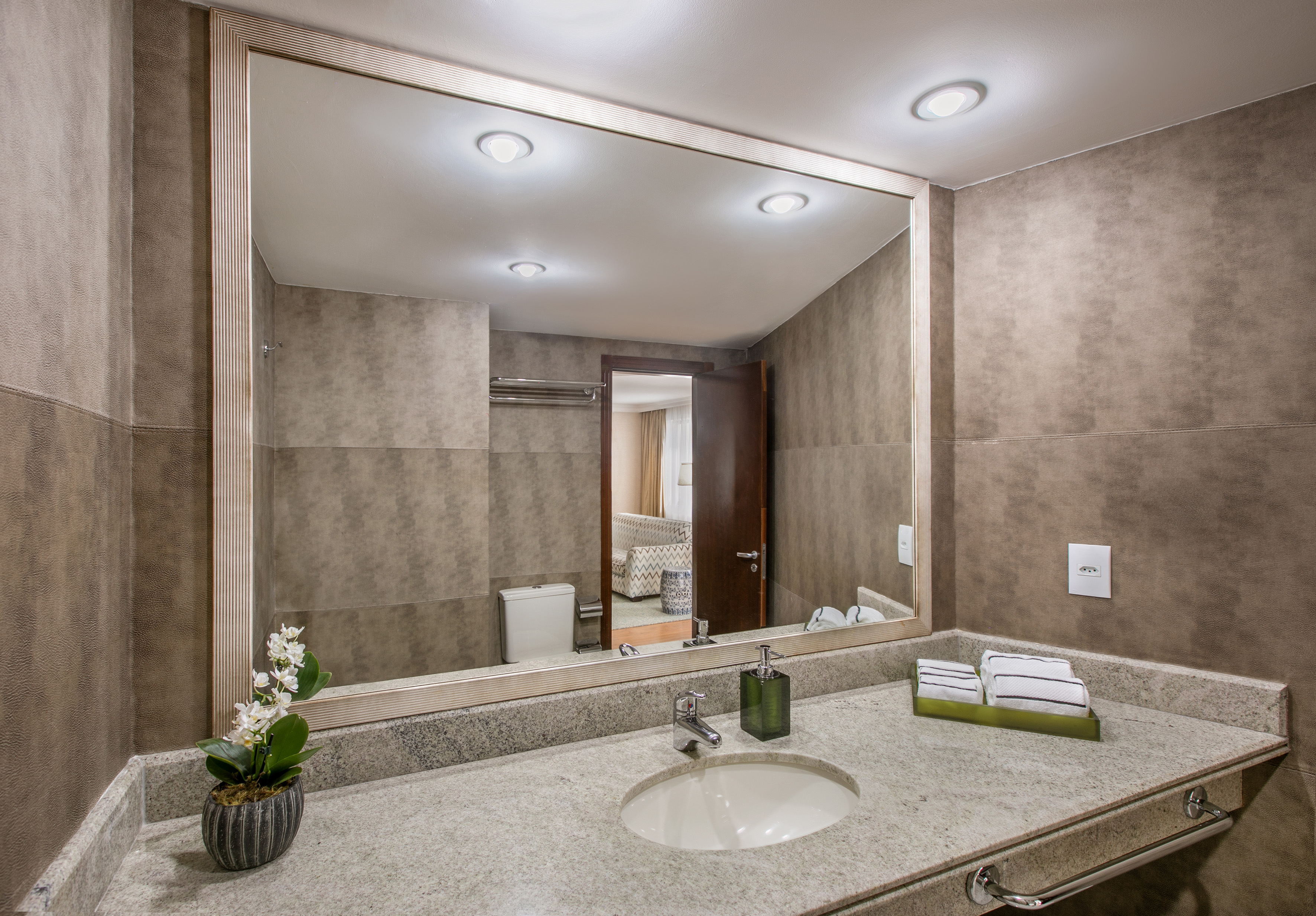 Modern hotel bathroom vanity with granite countertop, sink, large mirror, and tiled walls.