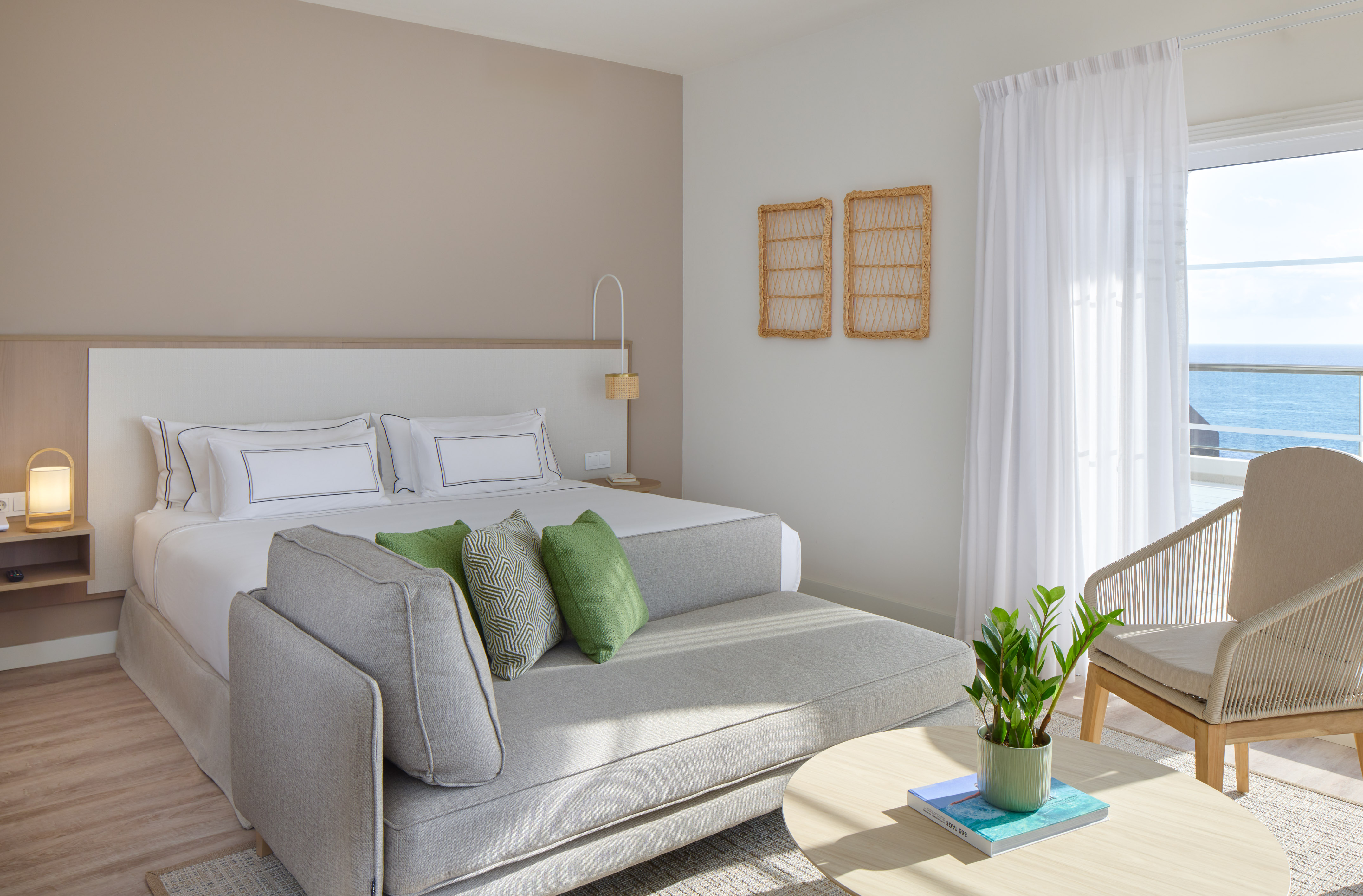 Modern hotel room with king bed, daybed, ocean view, and coastal decor.