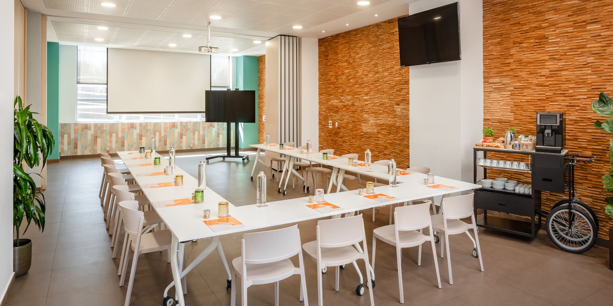 Modern conference room with U-shaped table, projector screen, and coffee station.