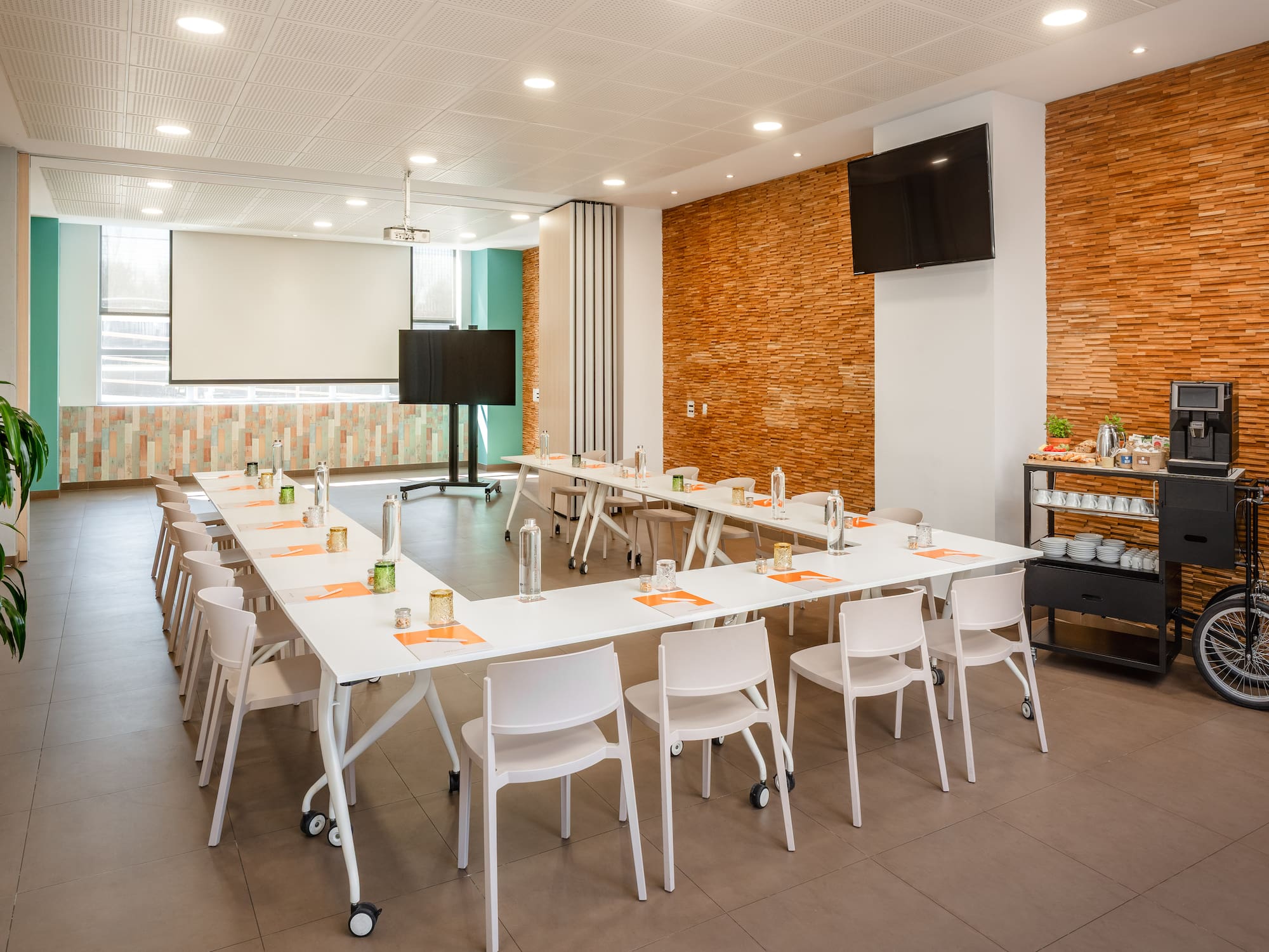 Modern meeting room with U-shaped table, projector screen, and coffee station.