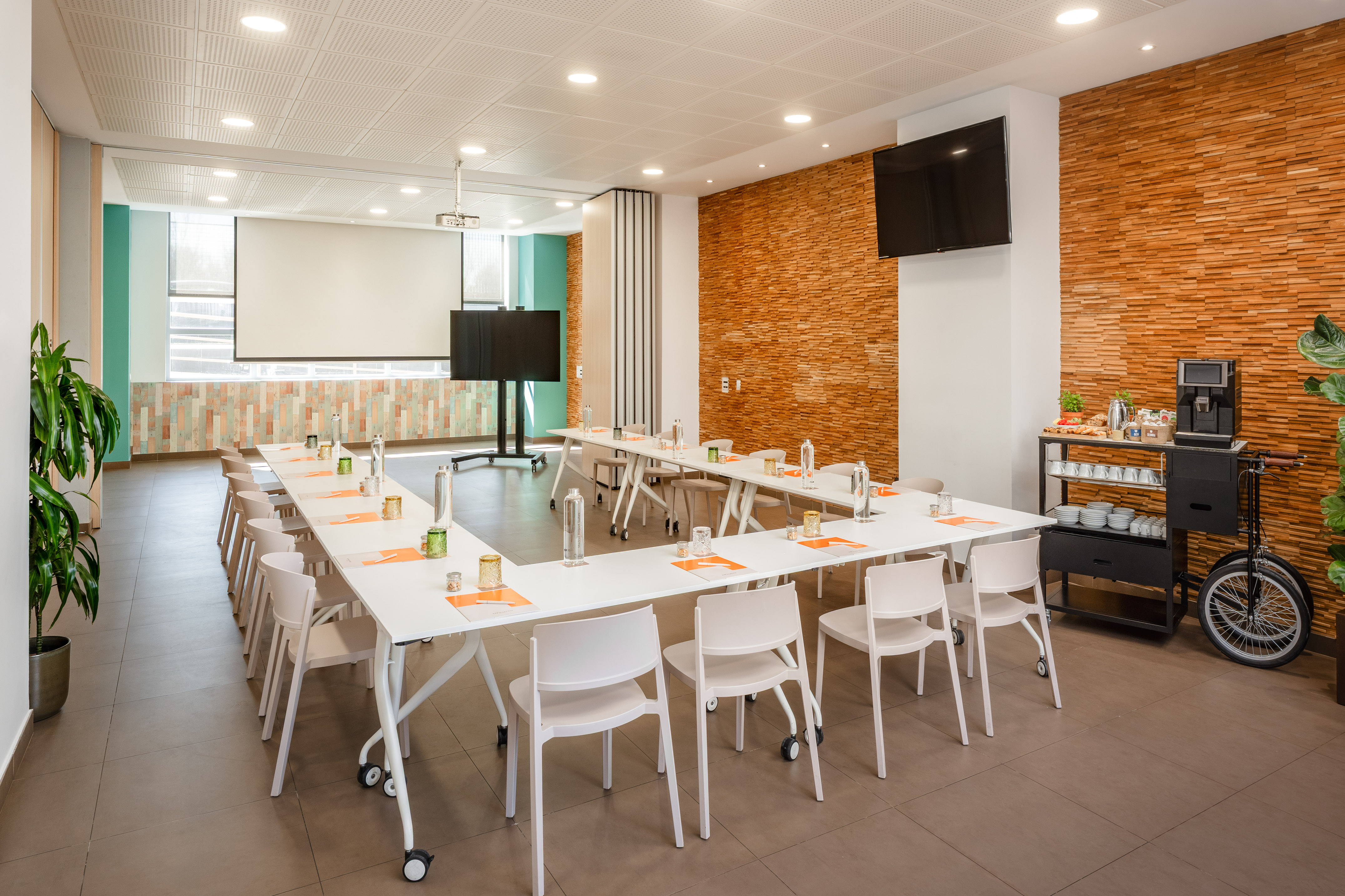 Modern conference room with U-shaped table, projector screen, and coffee station.