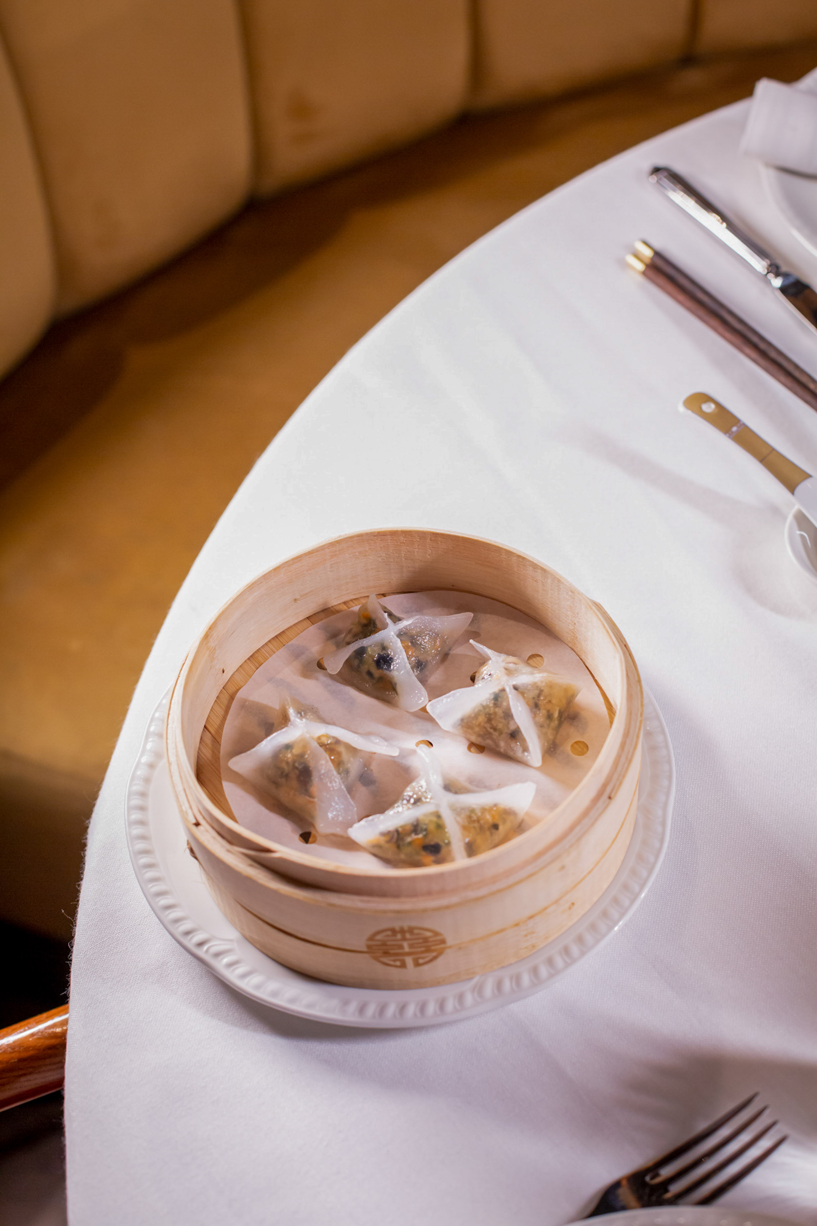 Four triangular dim sum dumplings in bamboo steamer on white restaurant table.