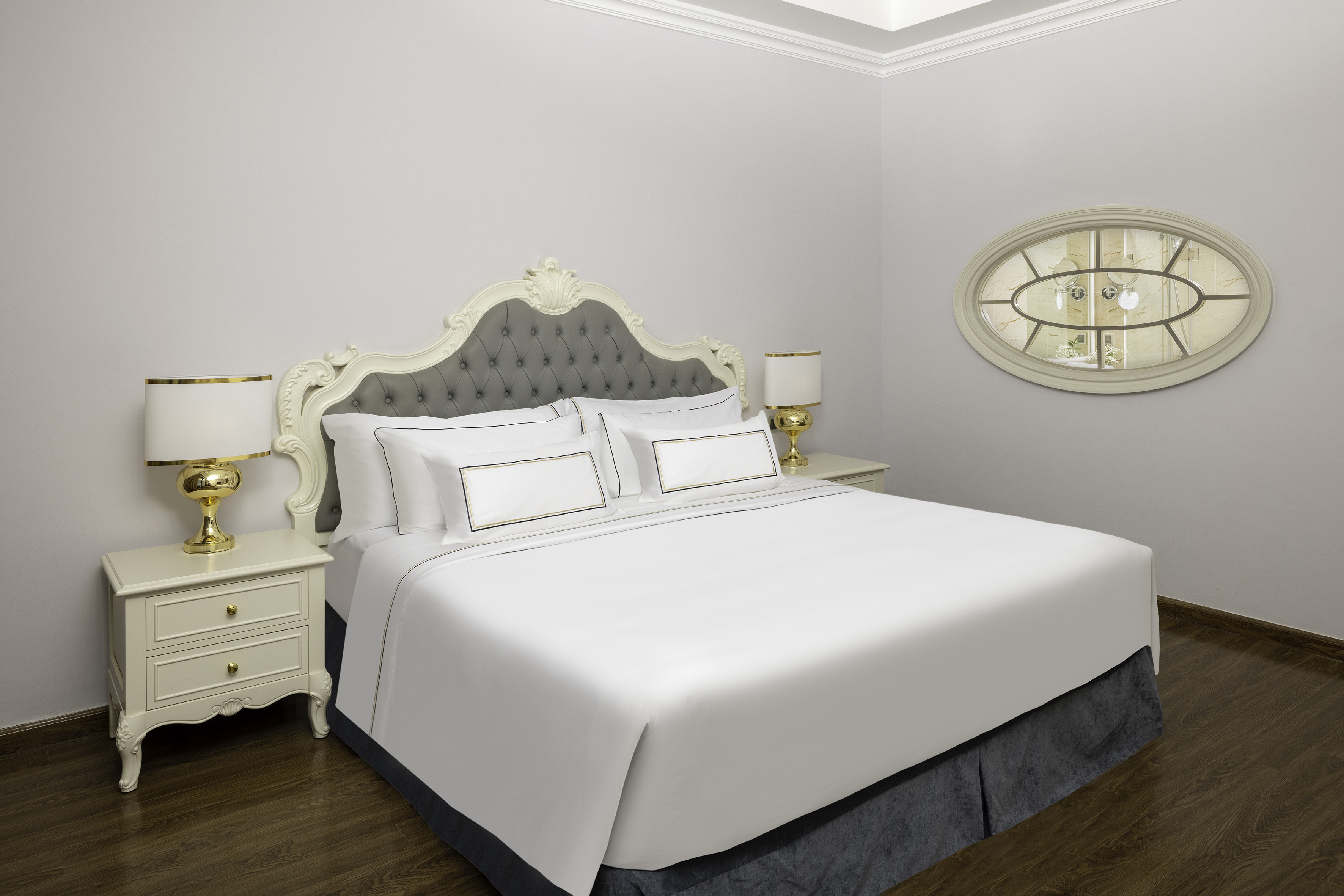 Luxury hotel room: tufted headboard, white bed, gold lamps, oval mirror.