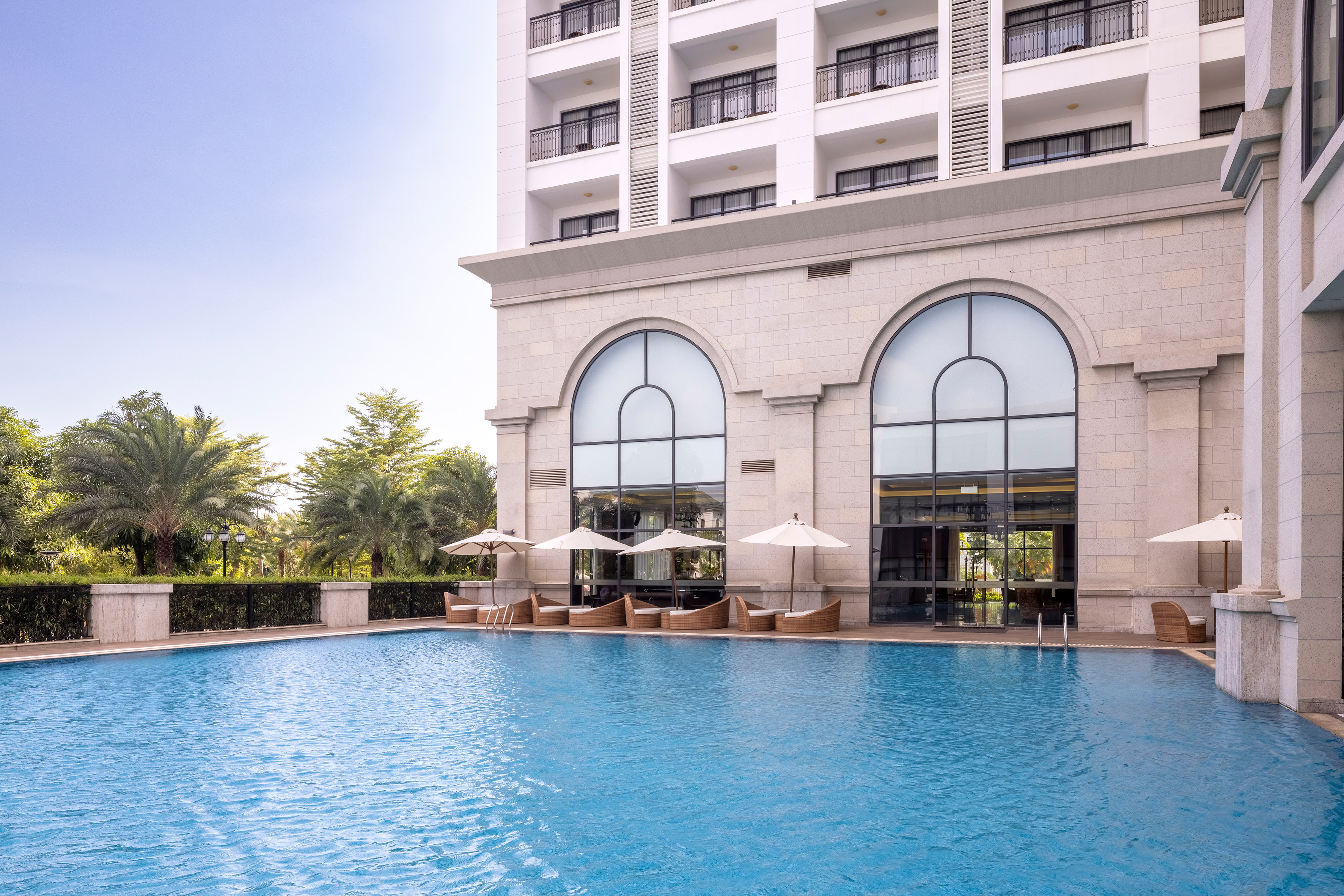 Luxury hotel with large outdoor swimming pool, sun loungers, and palm trees.