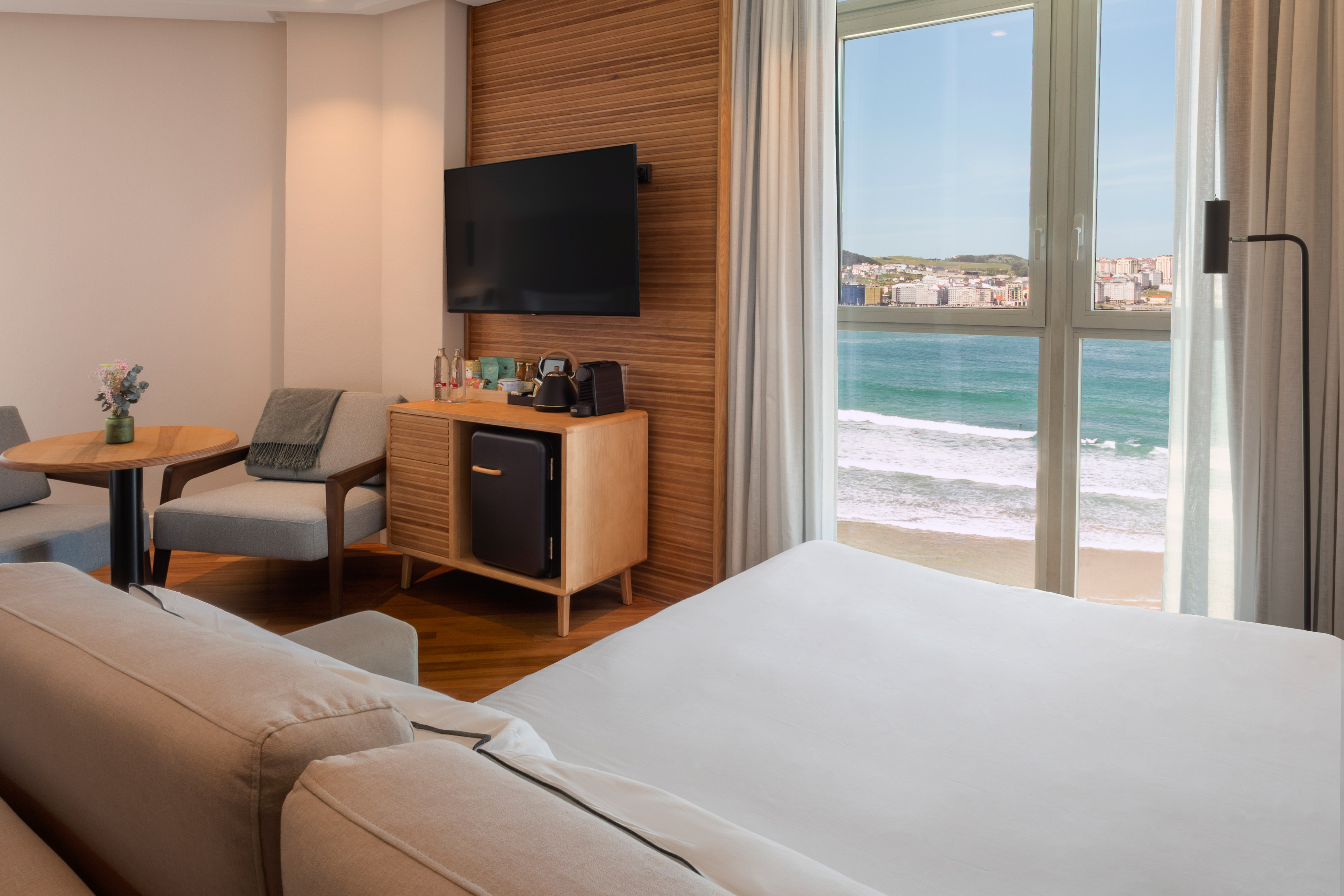 Coastal hotel room with ocean view, bed, sitting area, TV, and minibar.