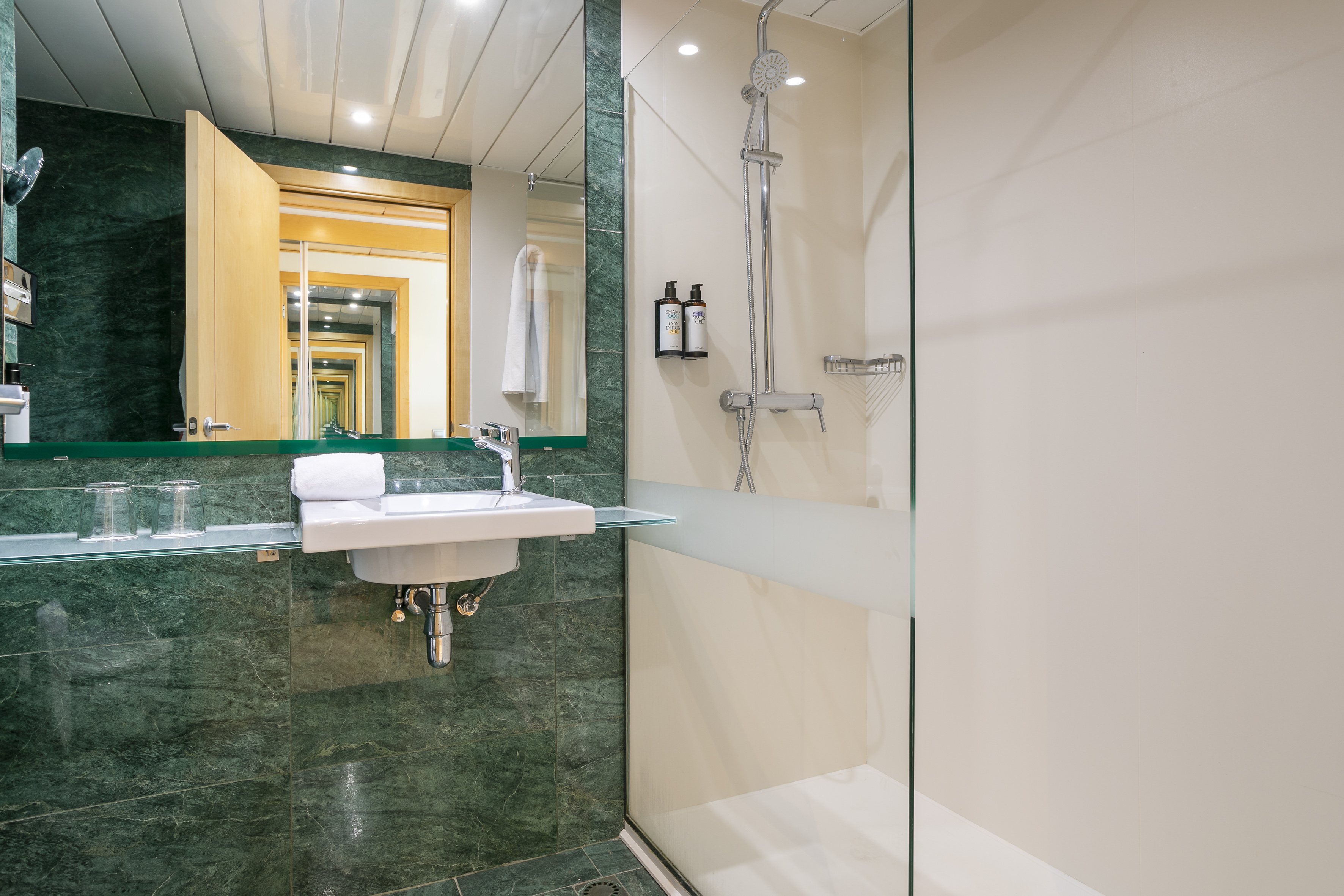 Modern hotel bathroom with green marble, white sink, and glass shower.