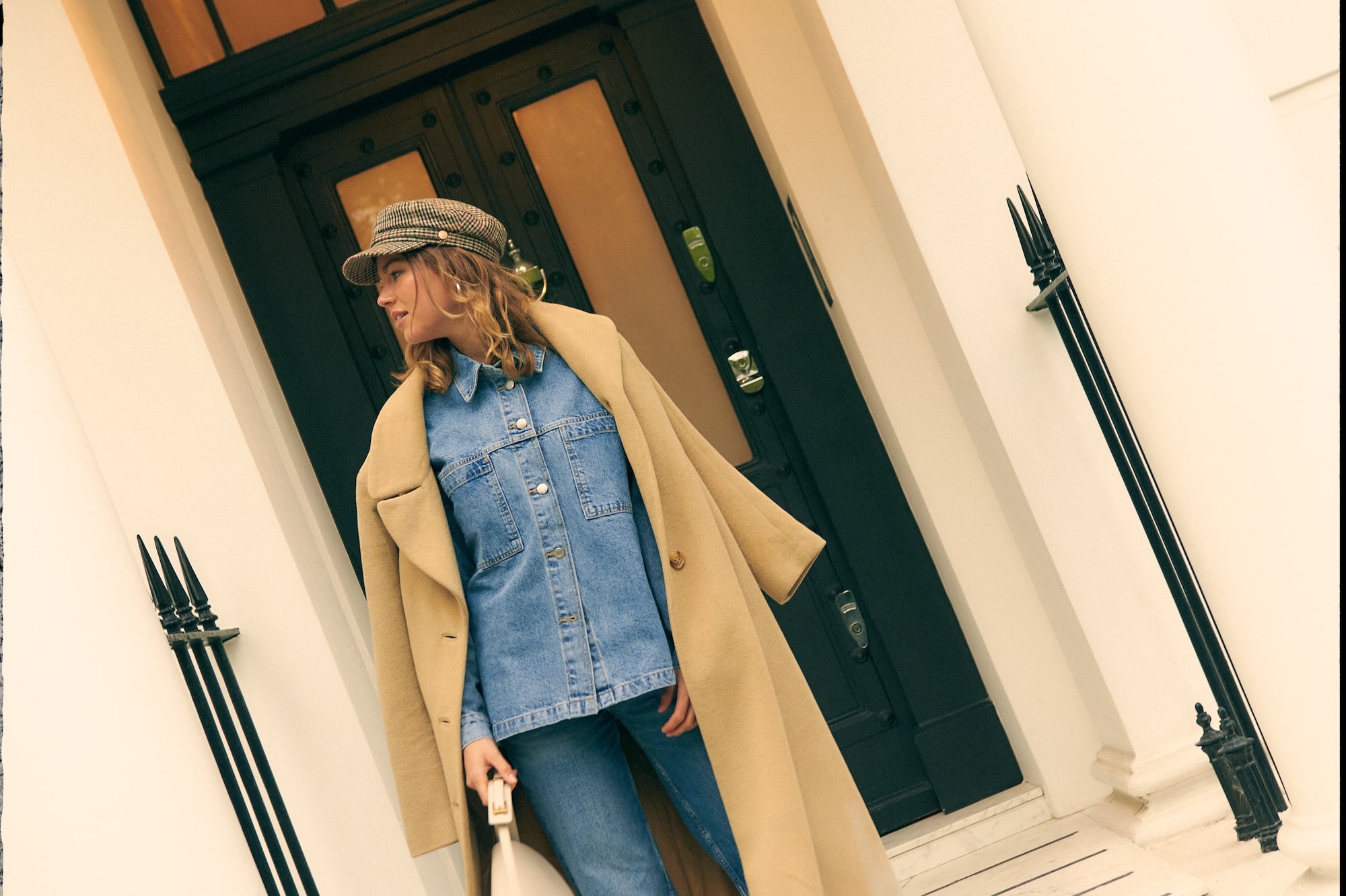 a woman in a hat and a long coat standing on a steps