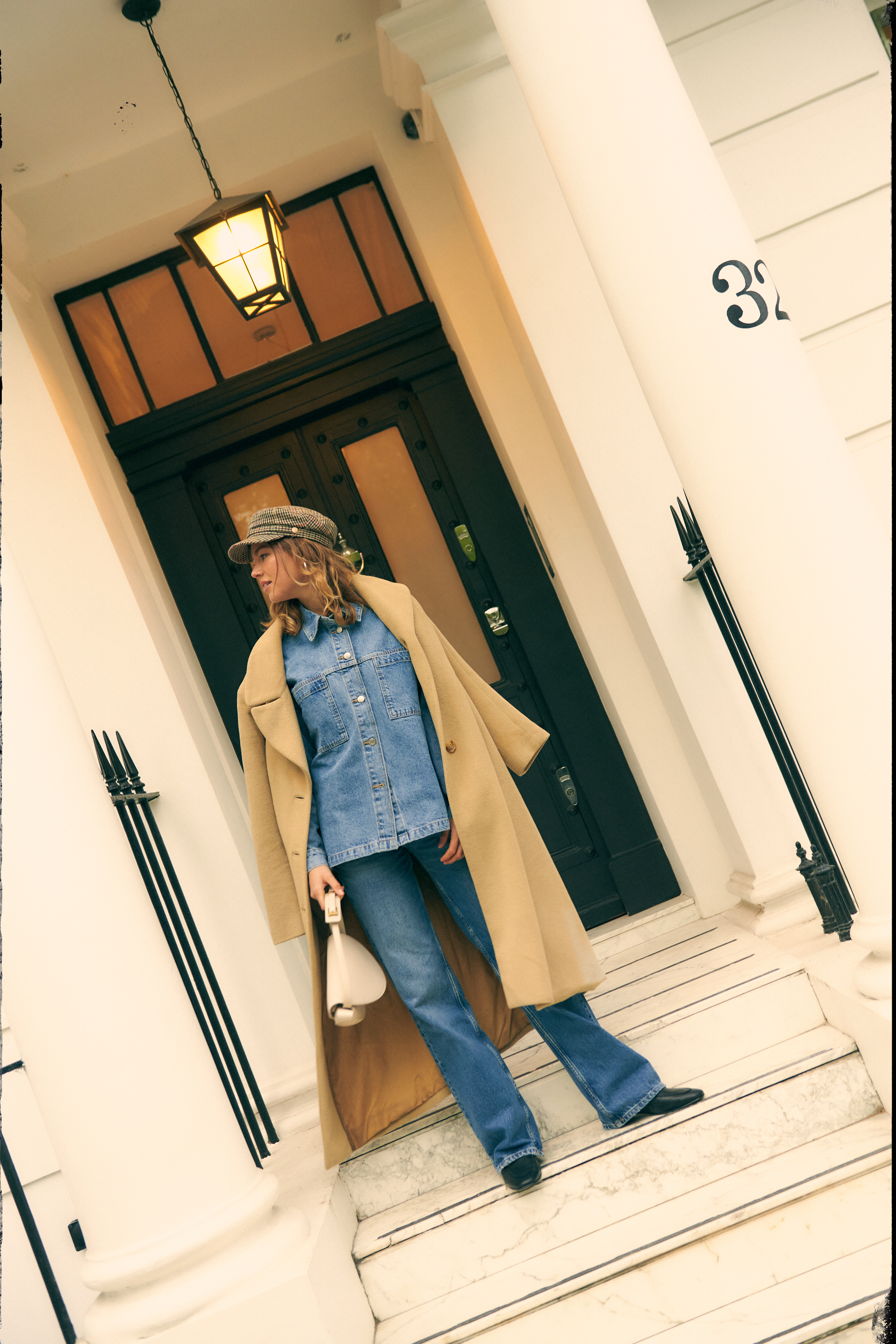 a woman in a hat and a long coat standing on a steps