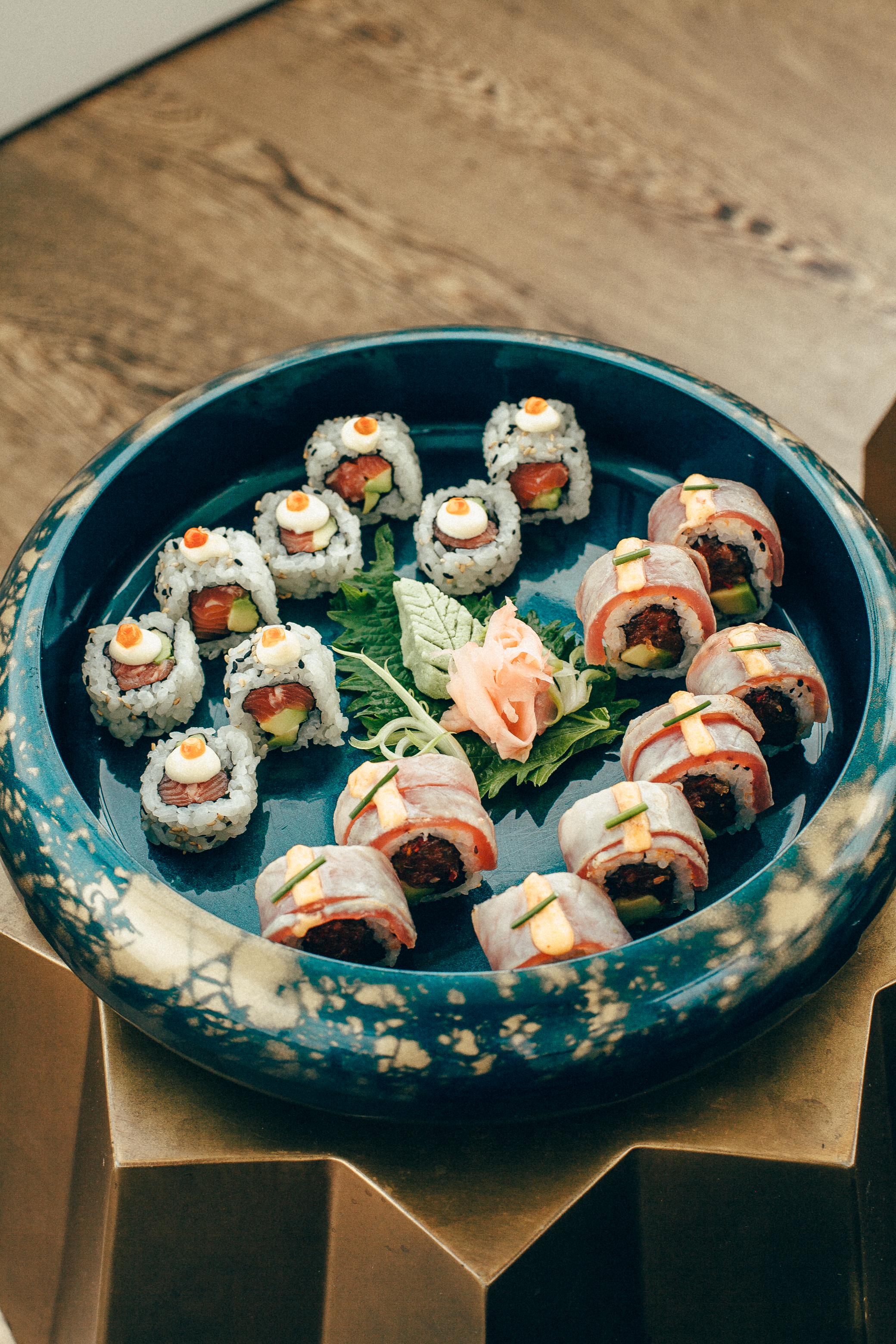 Assorted gourmet sushi rolls with tuna, salmon, avocado, and ginger in a blue bowl.