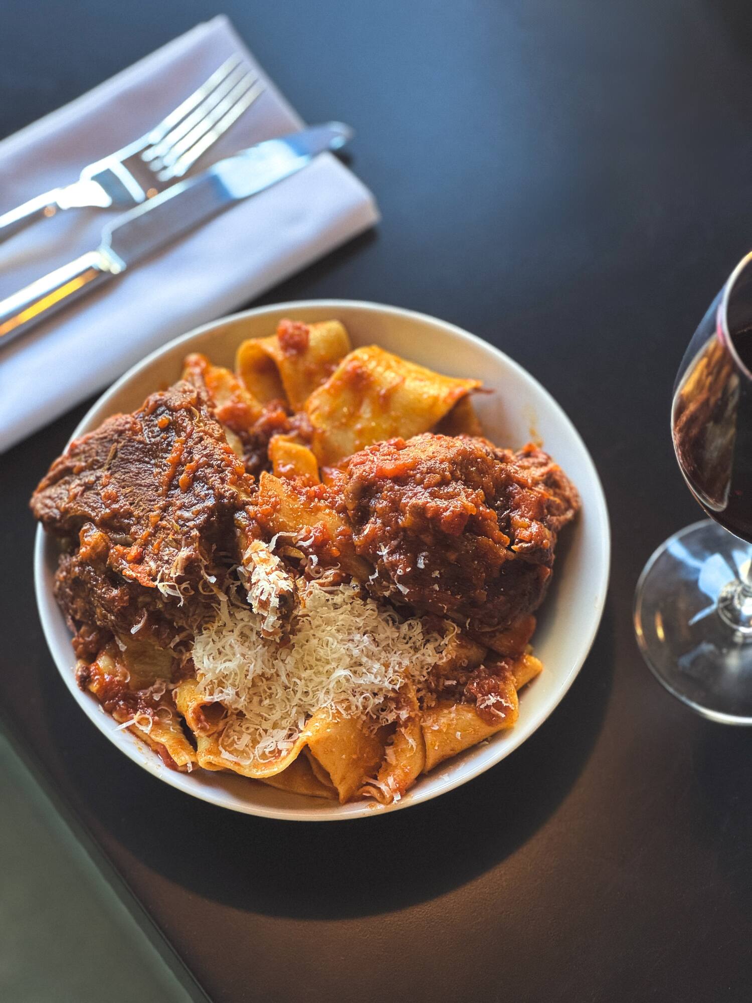 a plate of pasta and meat with cheese and a glass of wine