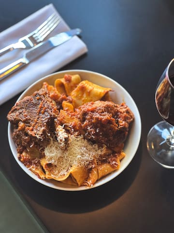 a plate of pasta and meat with cheese and a glass of wine