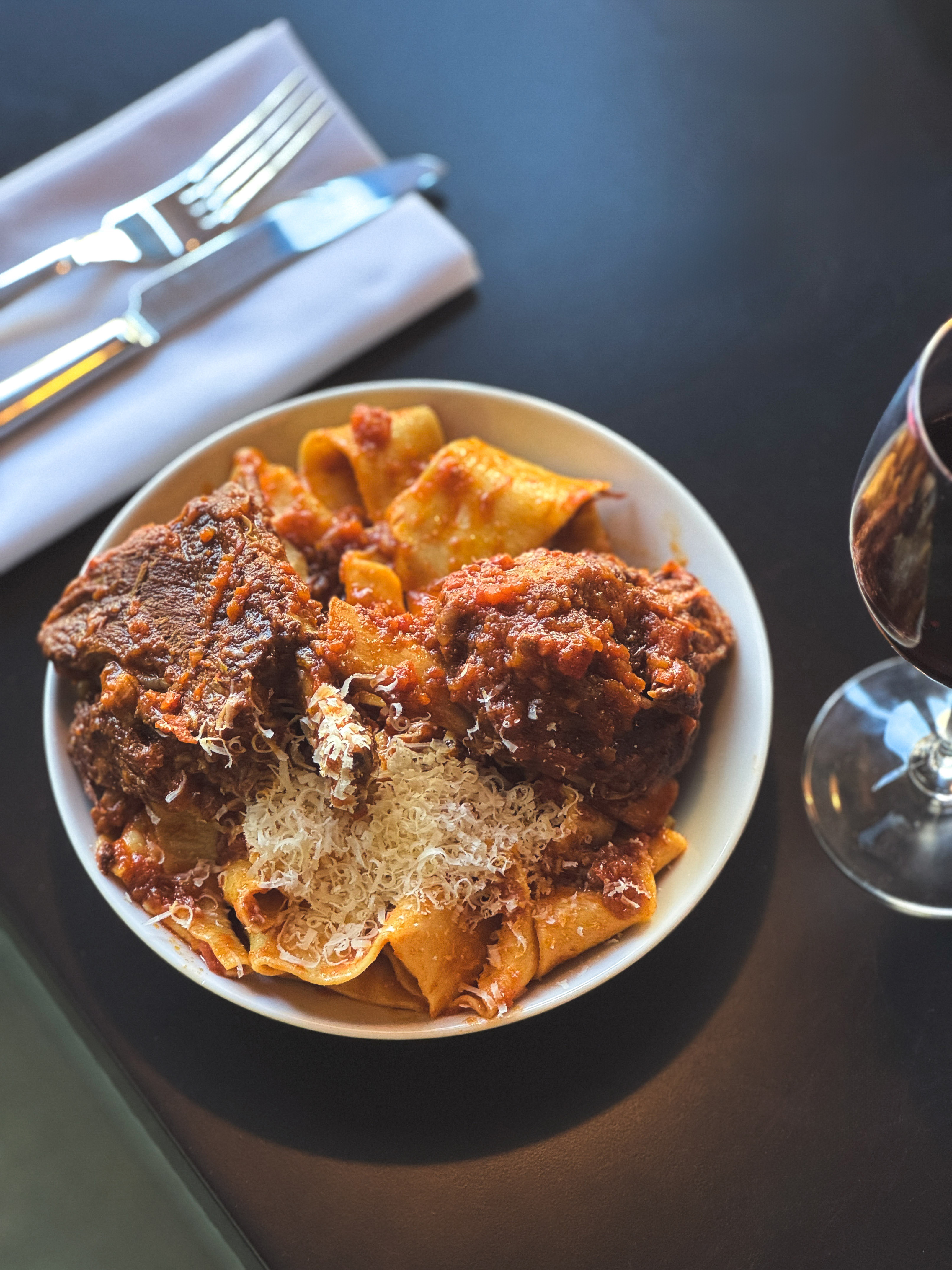 a plate of pasta and meat with cheese and a glass of wine