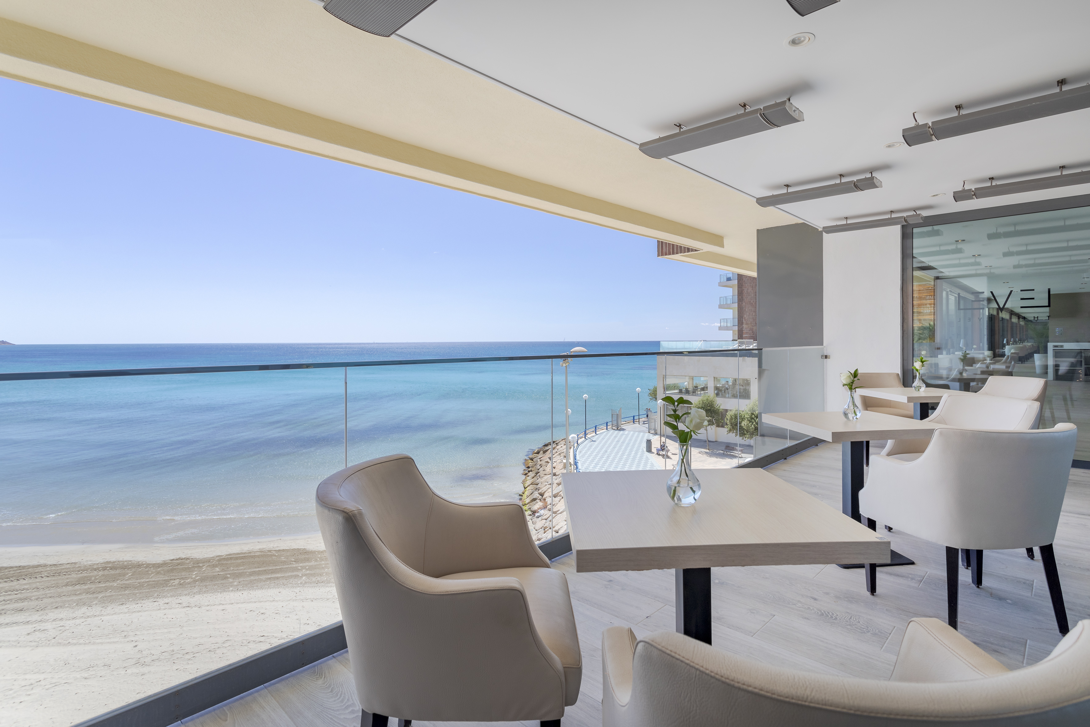 Coastal dining terrace with ocean view, sandy beach, and comfortable chairs.