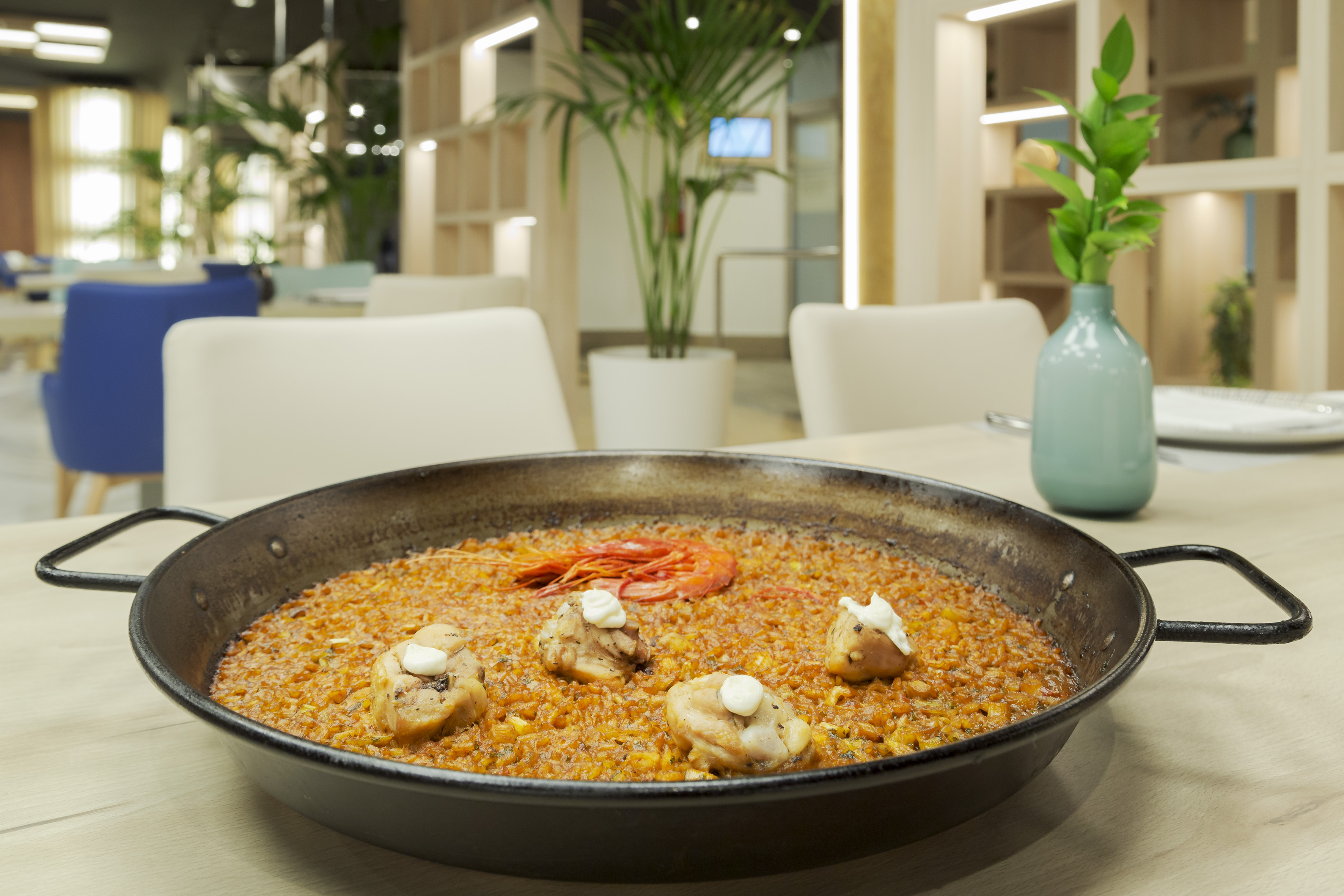 Golden paella with chicken and large shrimp in a restaurant dining room.