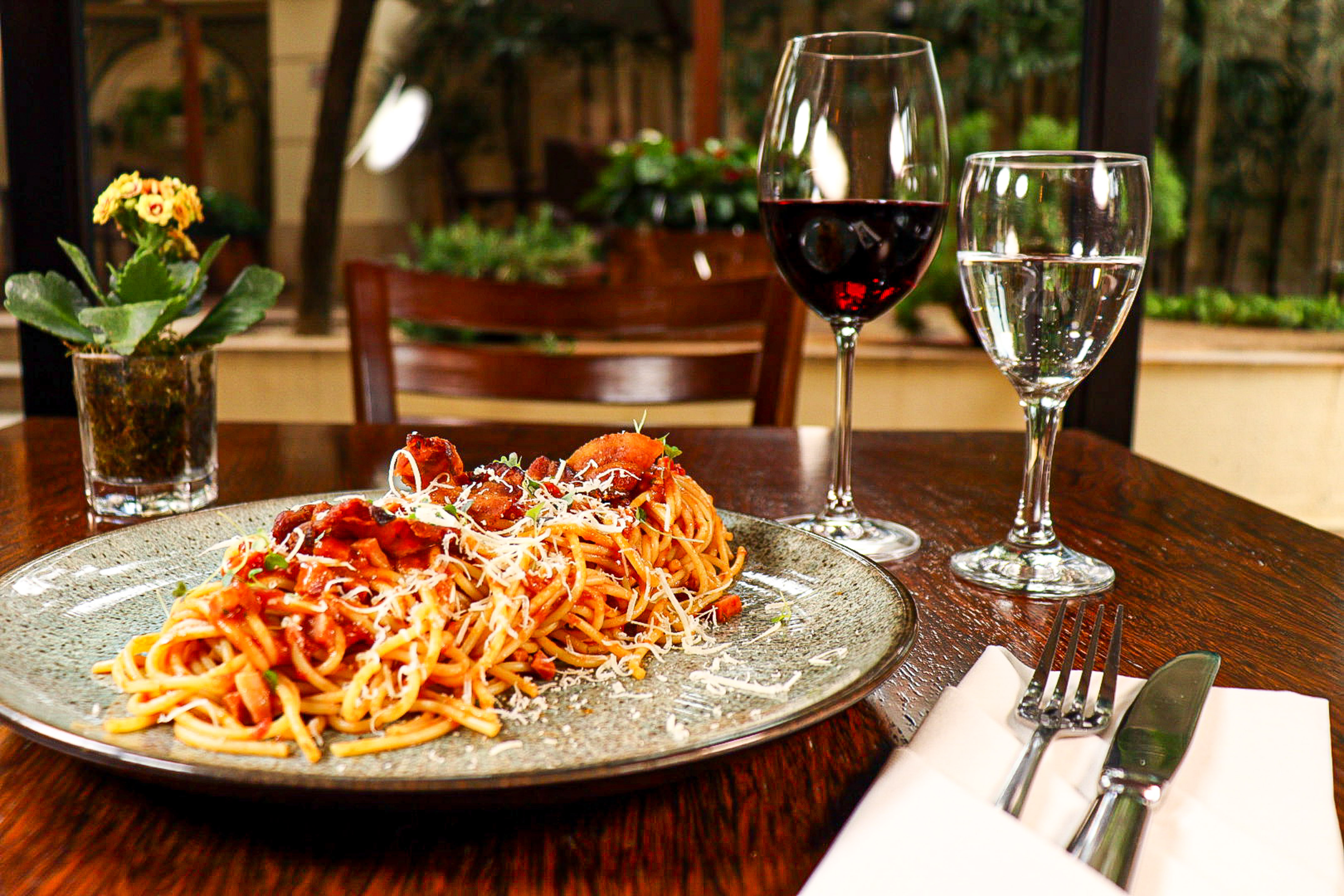 Italian spaghetti dinner with red wine, parmesan, and cutlery in a restaurant.
