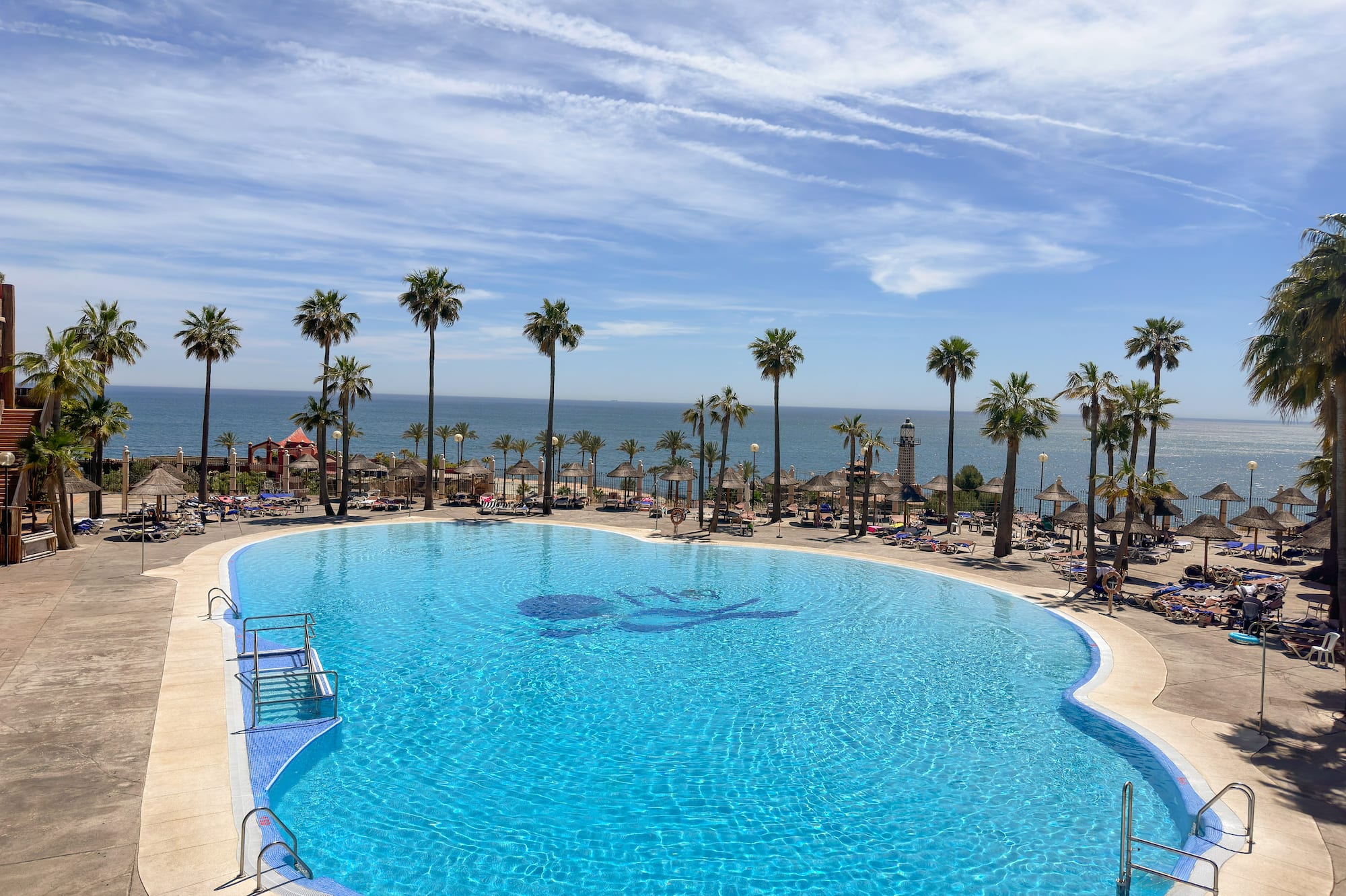 a pool with palm trees and a beach and a body of water