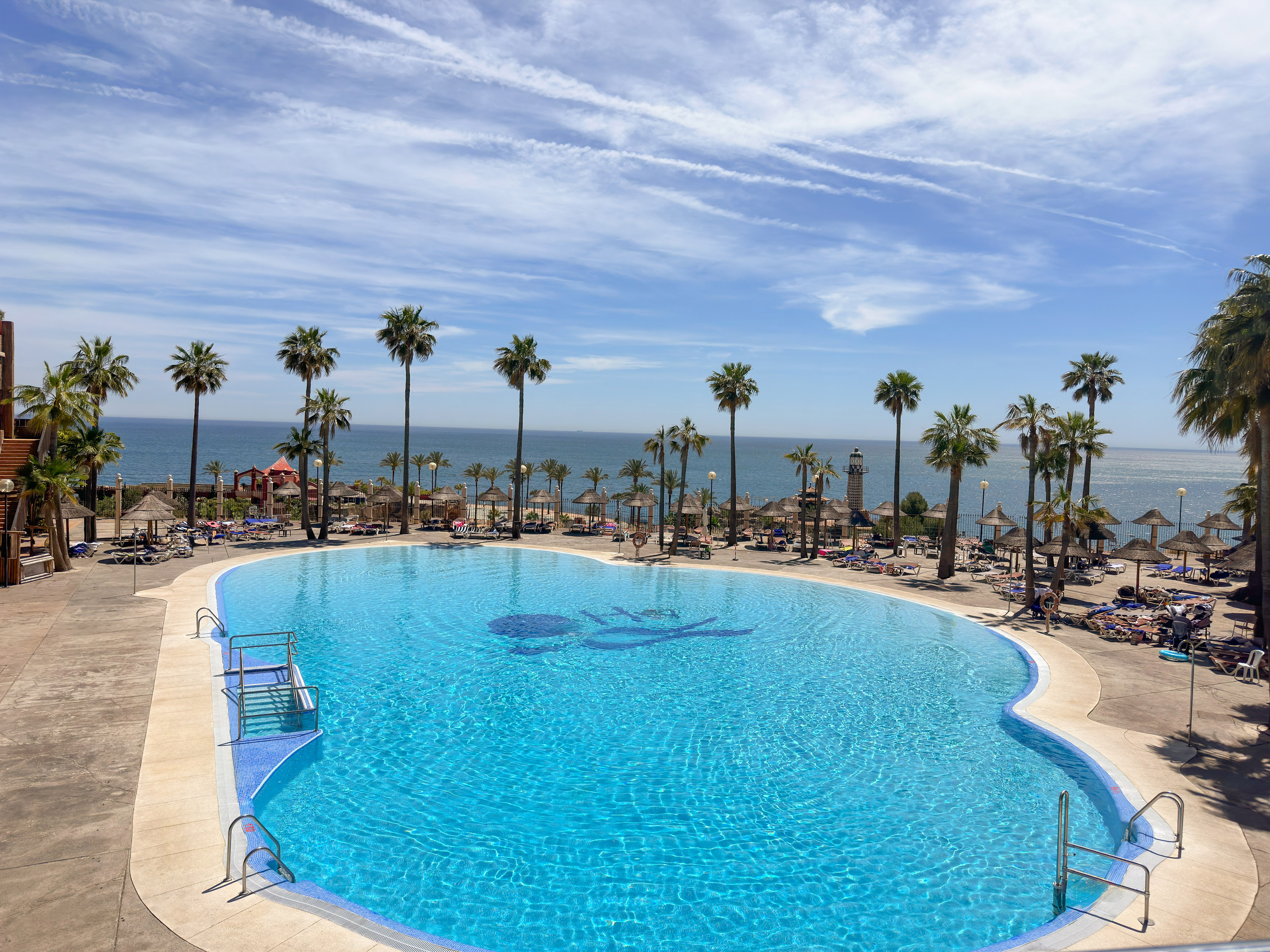 a pool with palm trees and a beach and a body of water