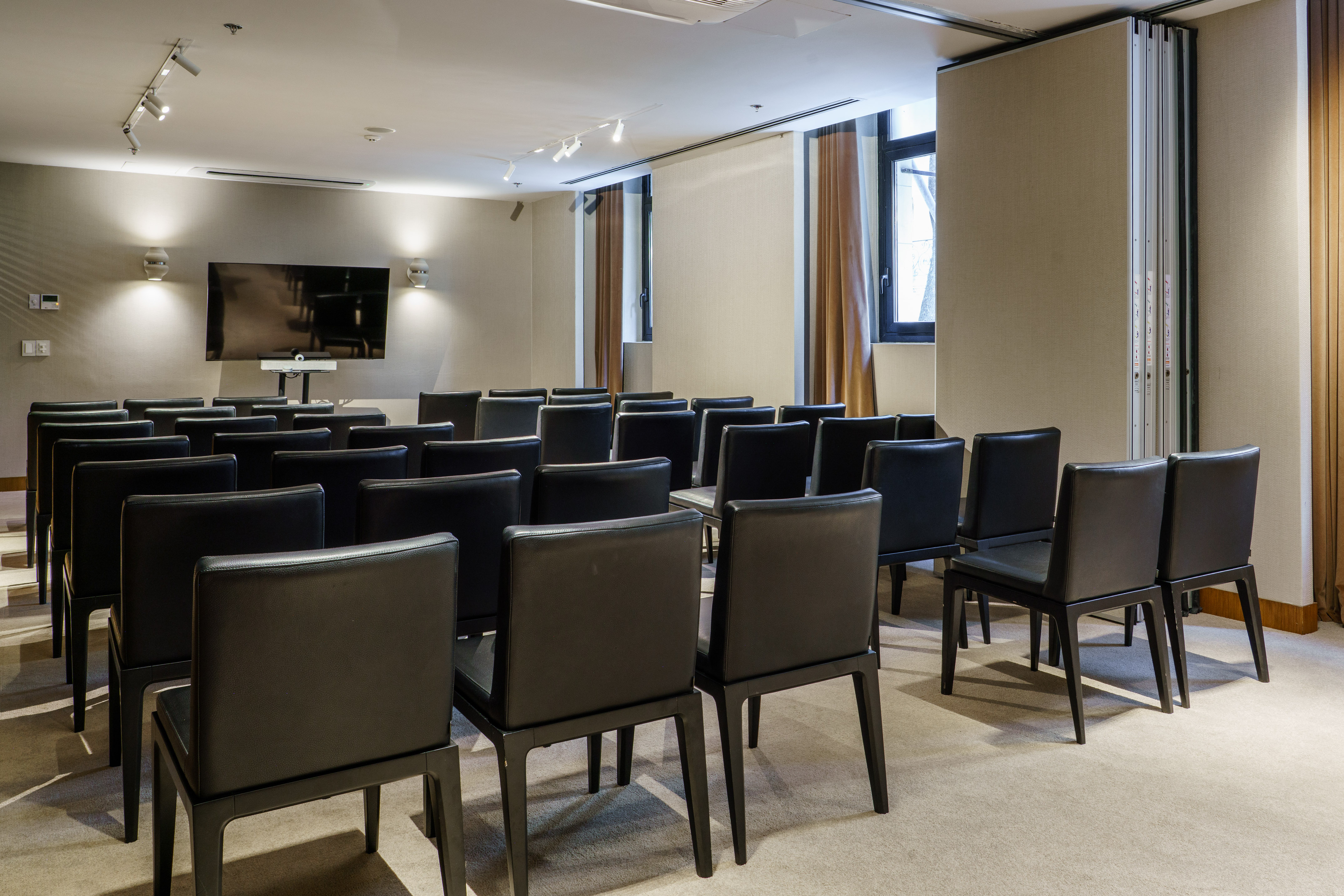 Modern meeting room with black chairs, large screen, and flexible partition walls.