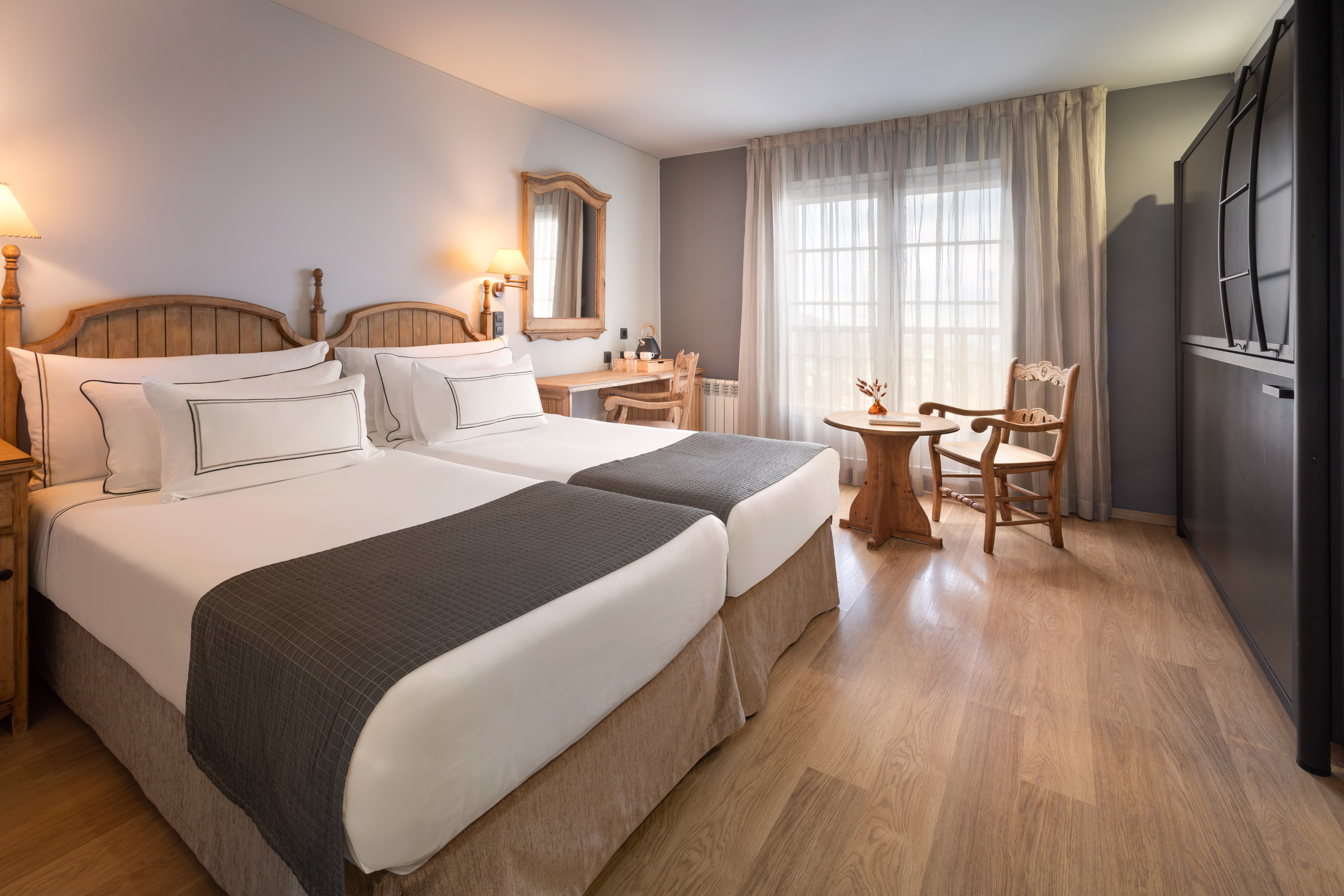 Rustic twin hotel room with wooden beds, desk, and cozy window nook.