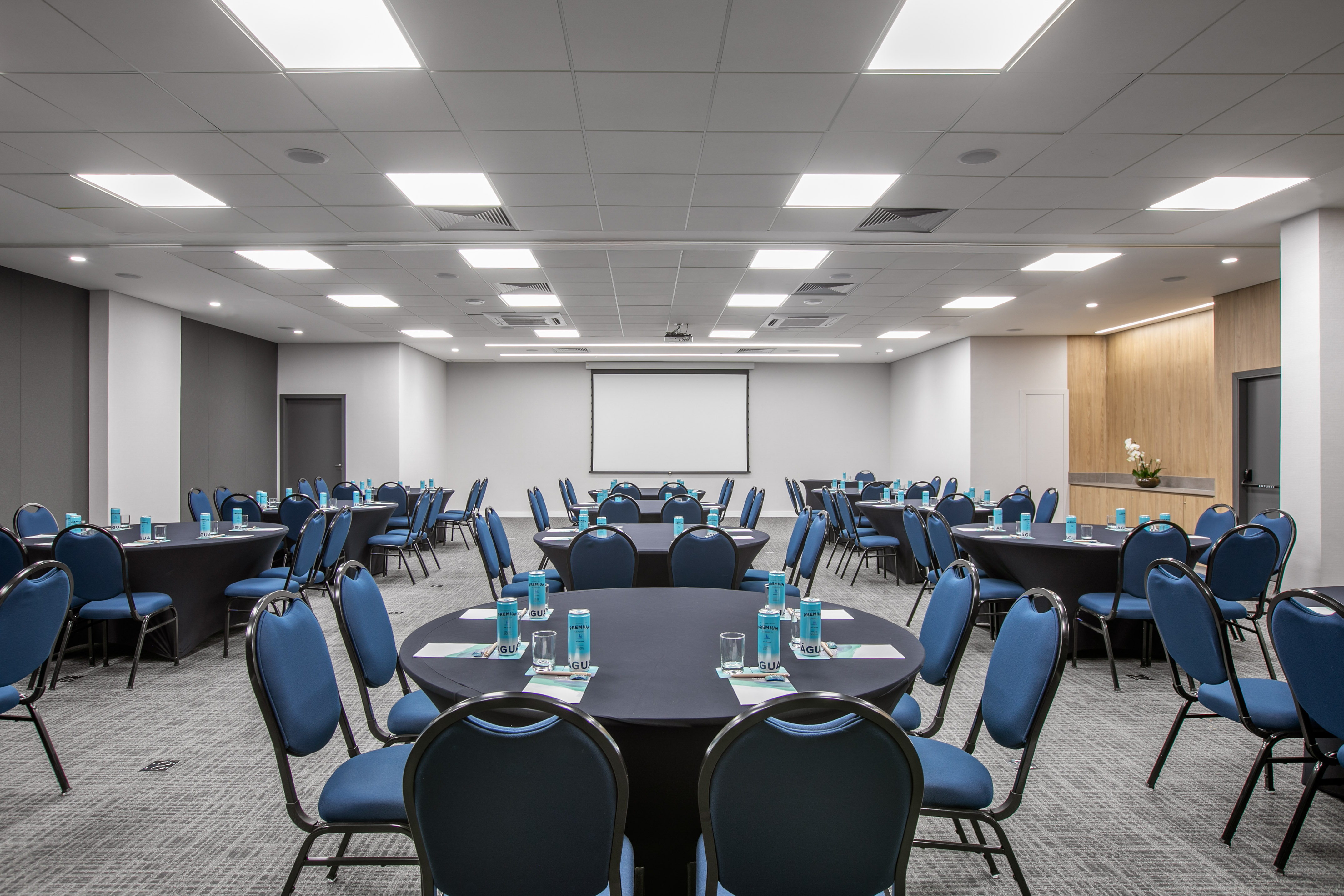 Spacious meeting room with round tables, blue chairs, and projector screen.
