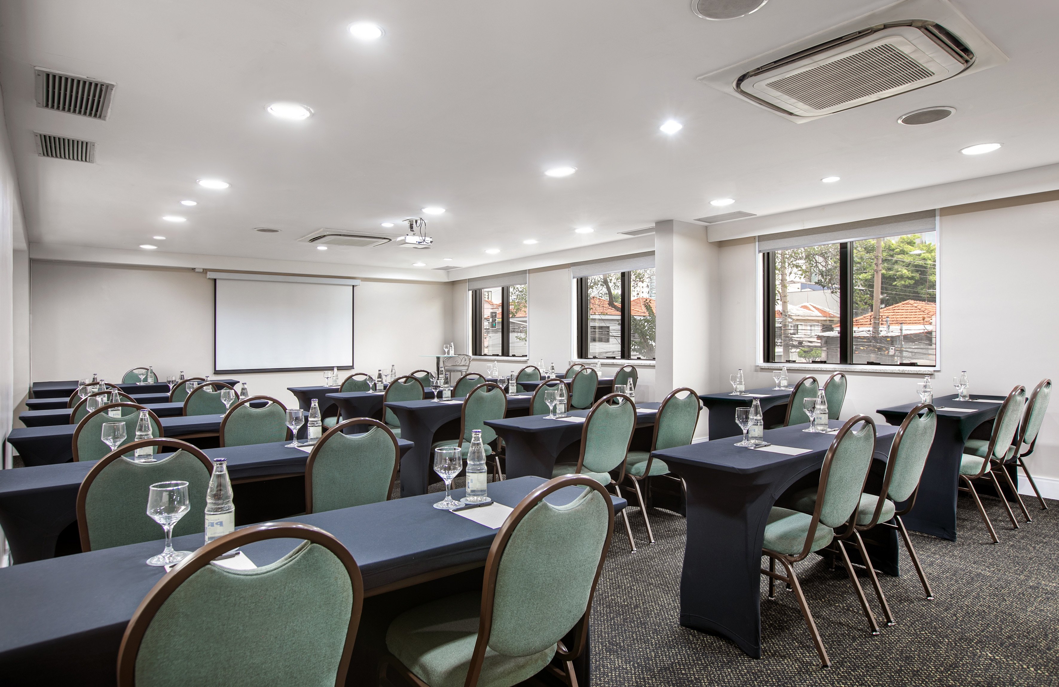 Professional conference room with green chairs, black tables, and a projection screen.