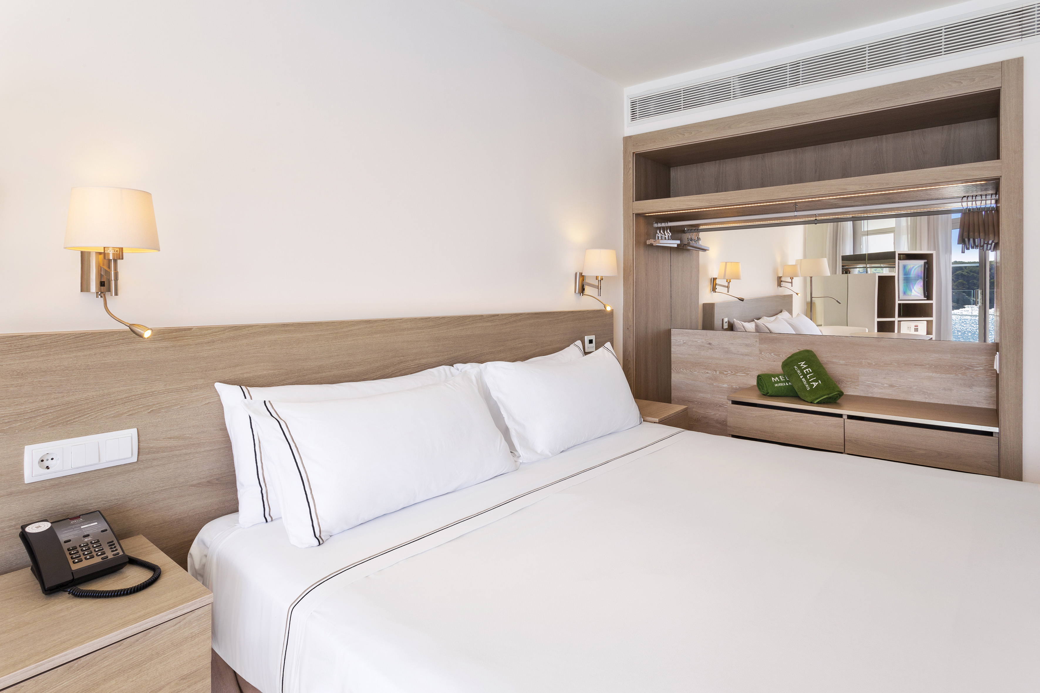 Meliá hotel room with white bed, wooden headboard, and large mirrored closet.