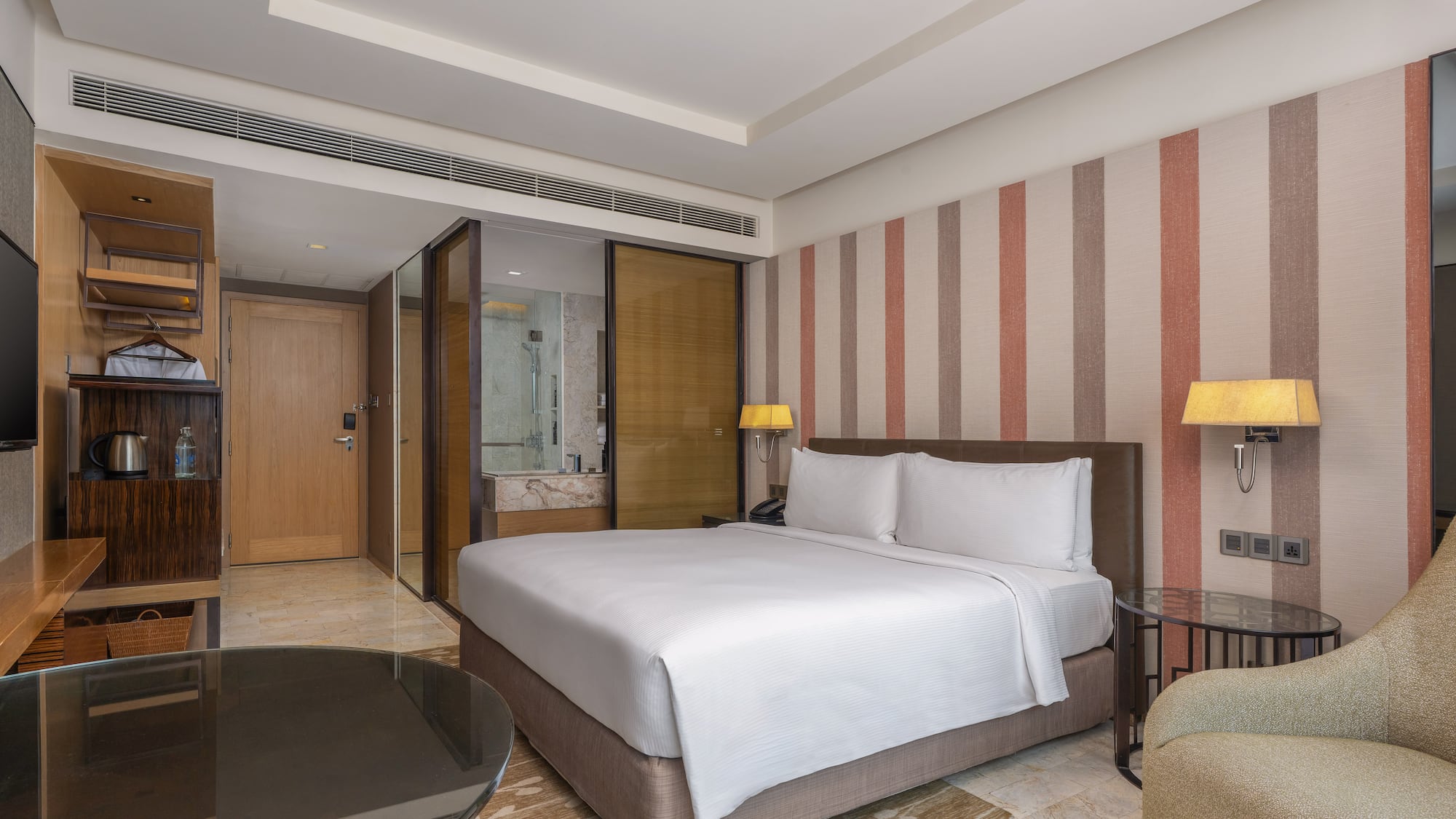 Modern hotel room with a king bed, striped accent wall, and glass-partitioned bathroom. - Guest Room - The Hotel Bangkok Sukhumvit 26 Affiliated by Meliá, بانكوك