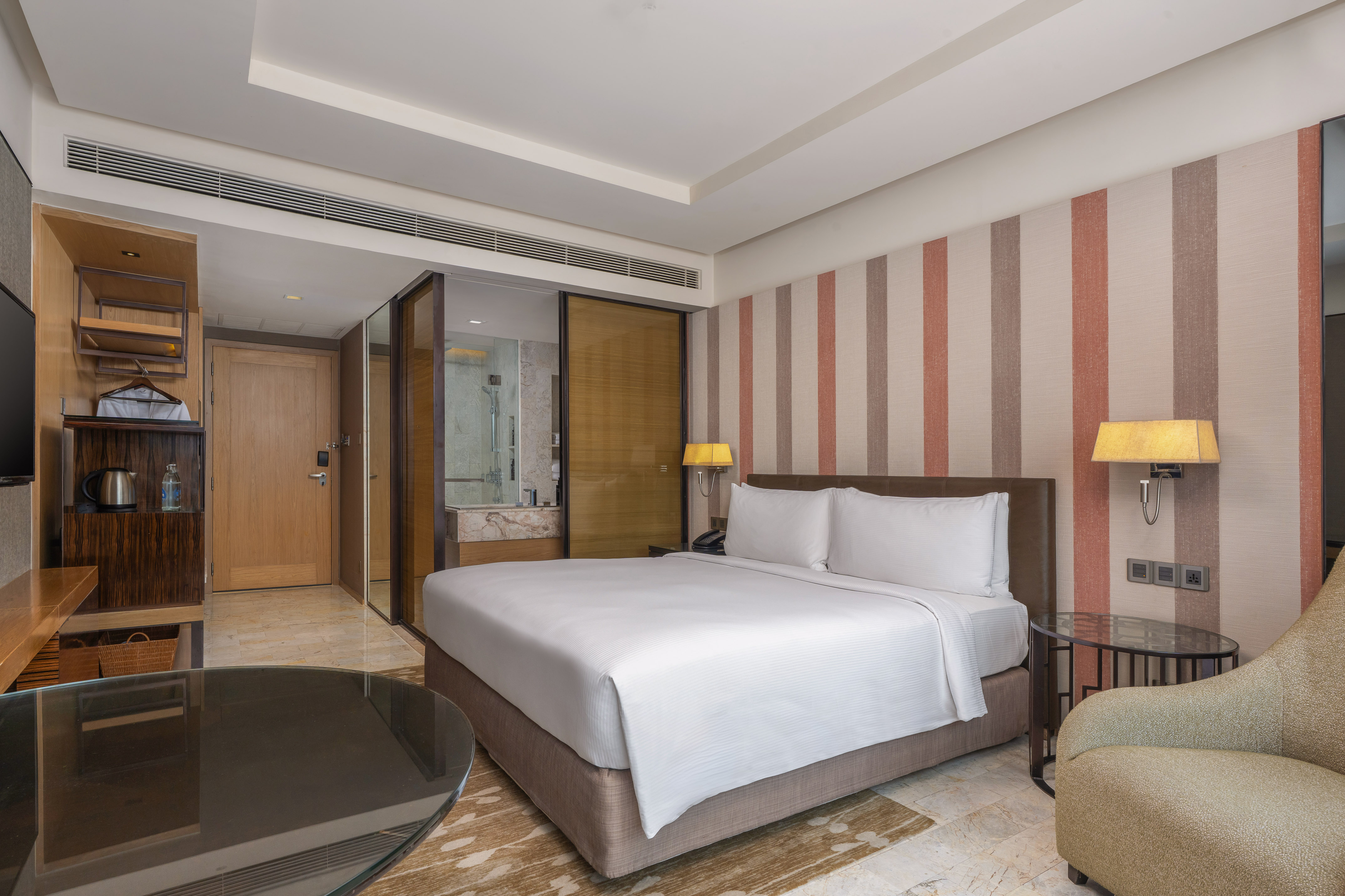 Modern hotel room with a king bed, striped accent wall, and glass-partitioned bathroom. - Guest Room - The Hotel Bangkok Sukhumvit 26 Affiliated by Meliá, بانكوك