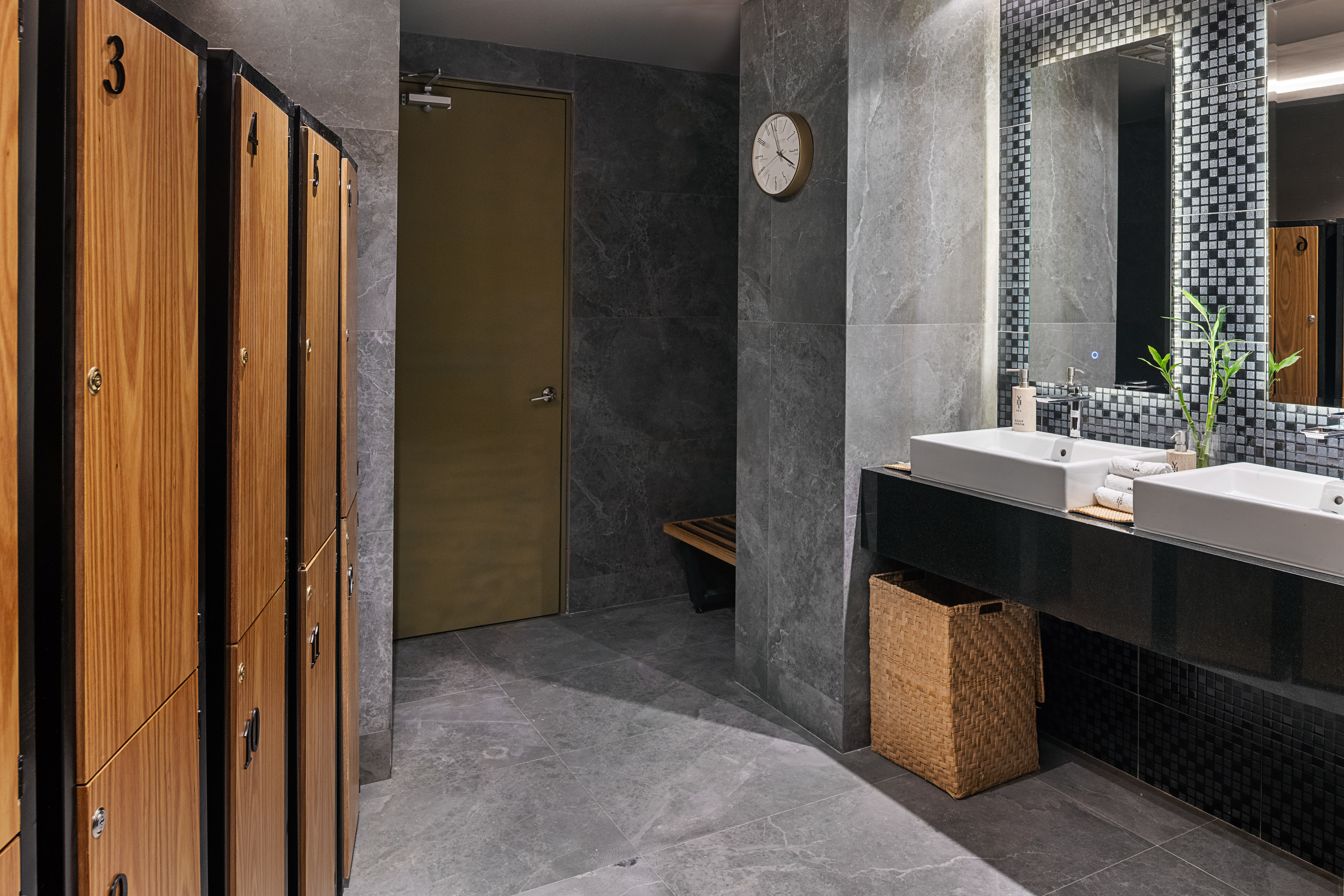 Modern gym changing room with wood lockers and dual vanity sinks.