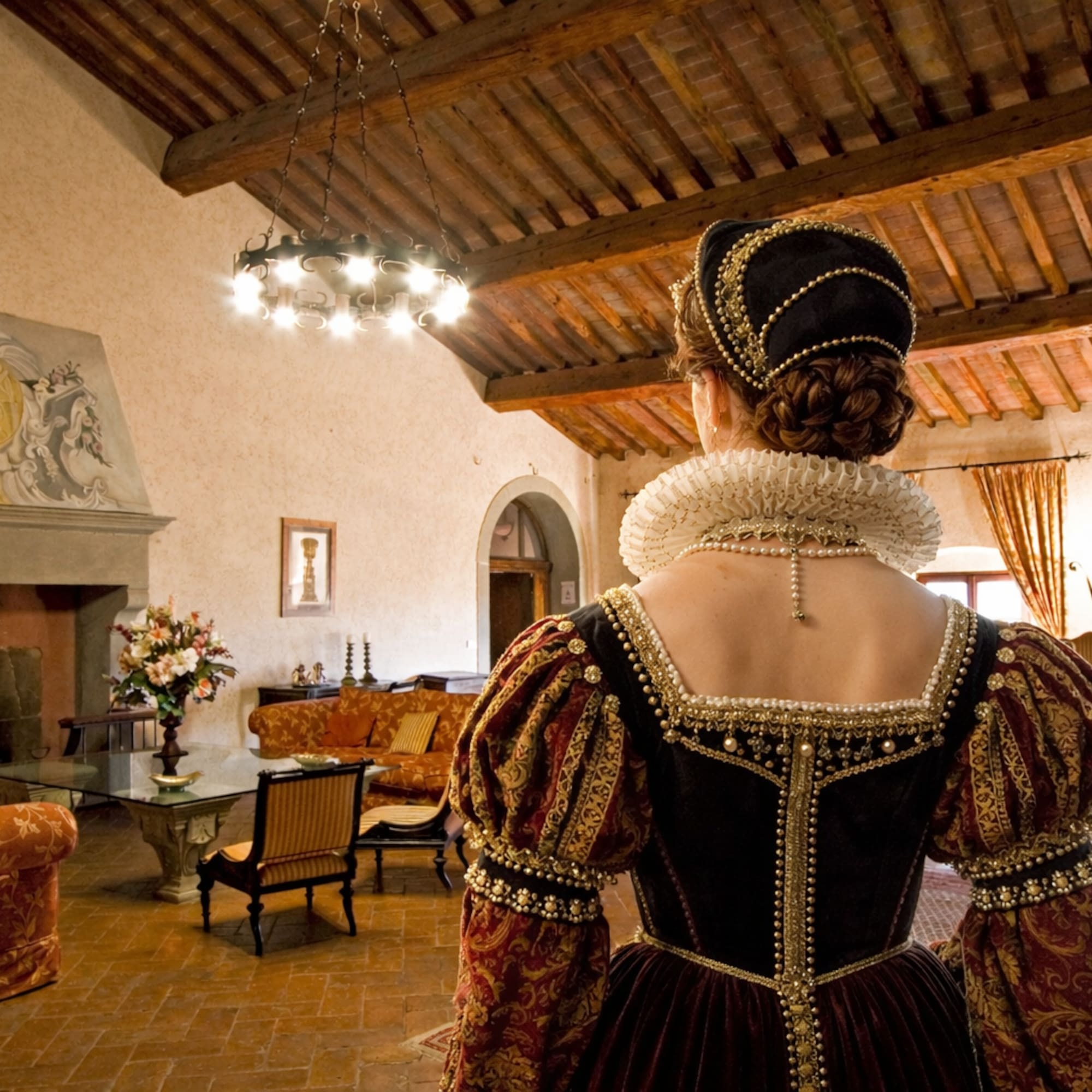 Woman in elaborate Renaissance costume, viewing a grand historic villa interior.
