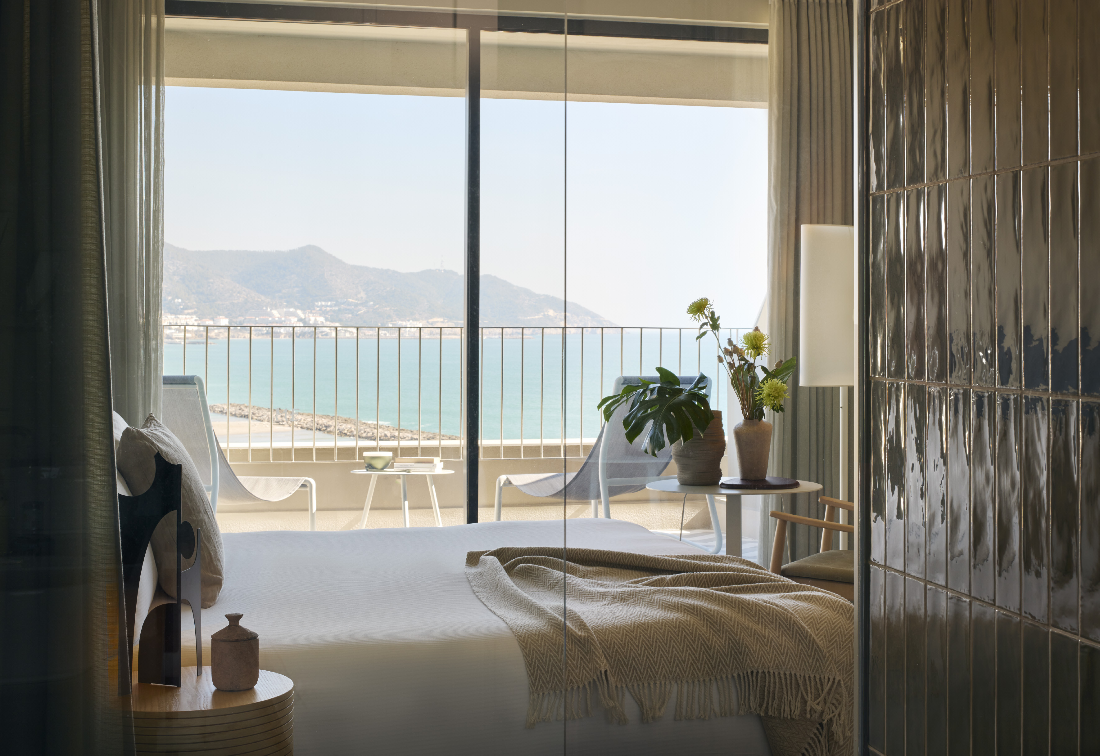 Modern hotel bedroom with balcony, ocean view, and distant mountains.