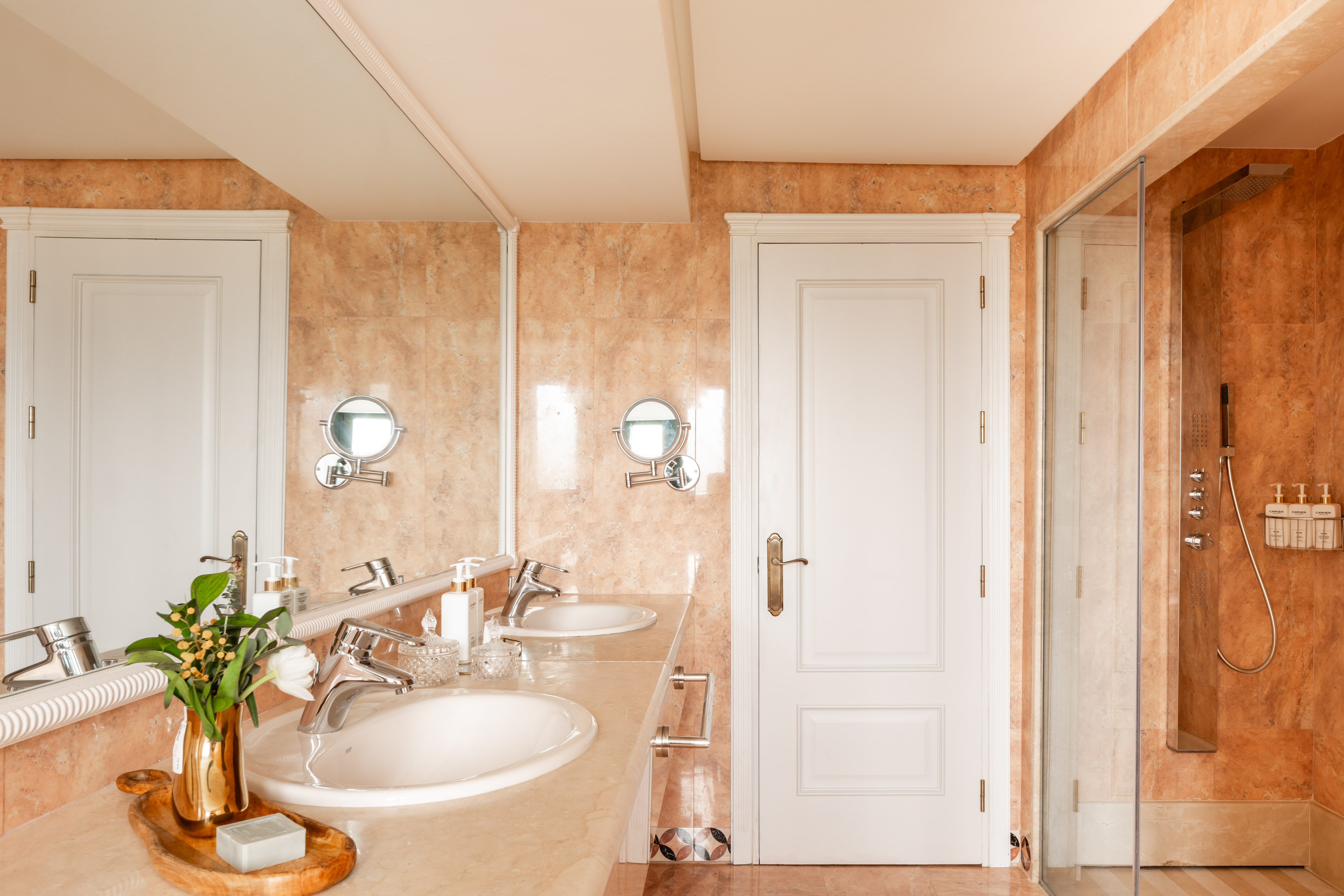 Hotel bathroom featuring double sinks, marble vanity, and tiled shower.